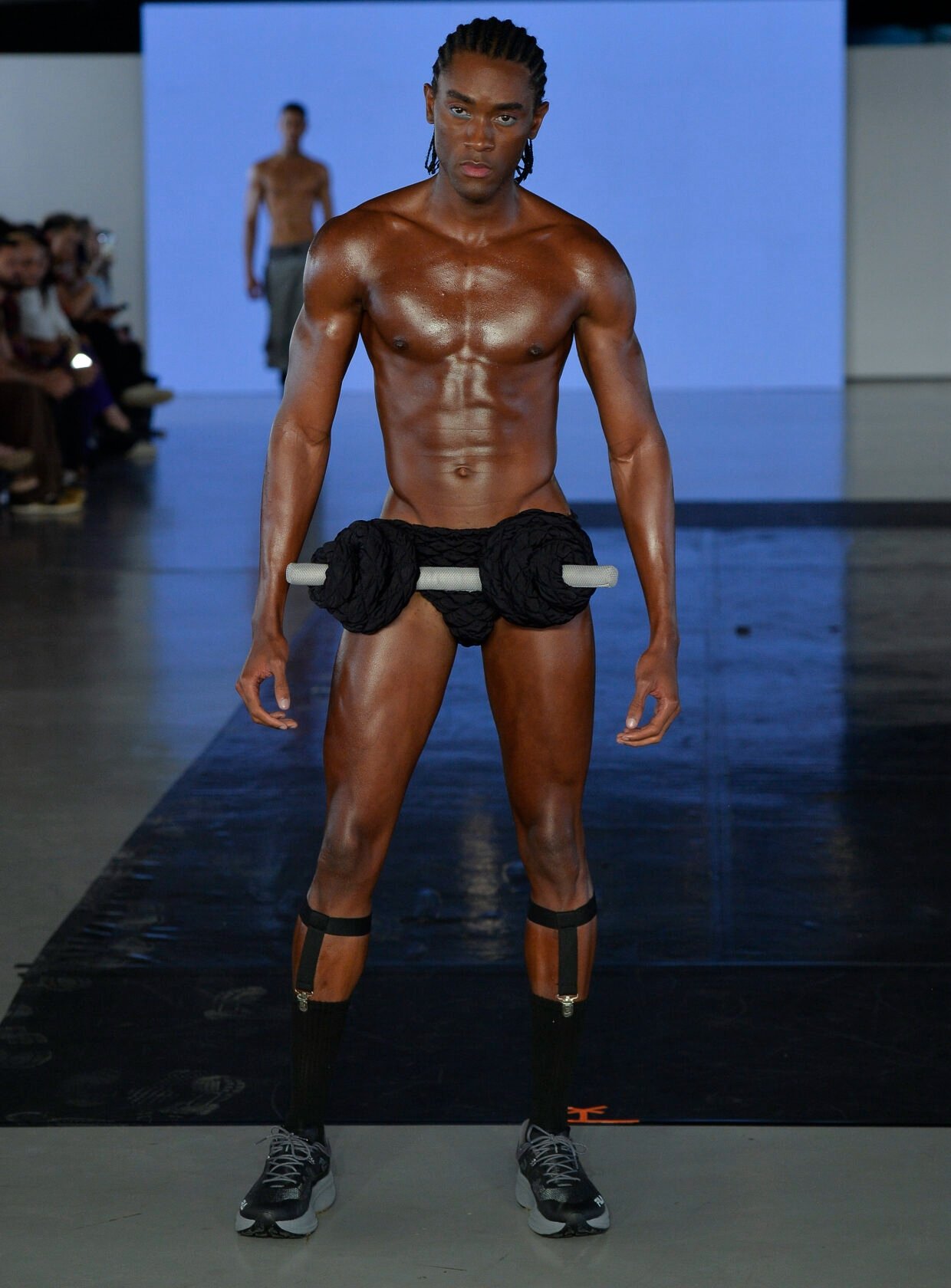 Modelo masculino posa firme e confiante na Casa de Criadores 57 com peça preta trançada e barra rígida, meias pretas com