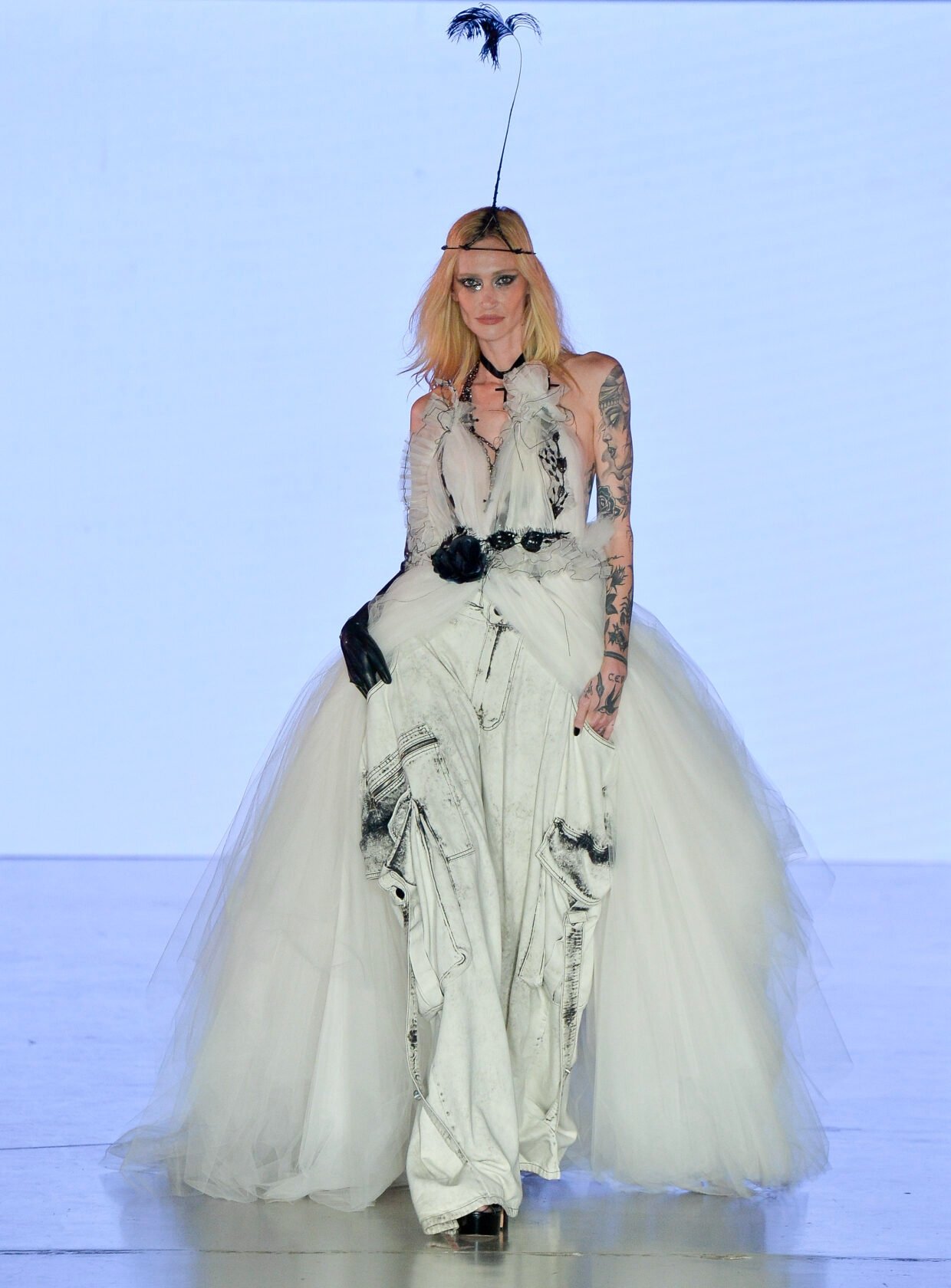 Modelo caminha com vestido branco de tule volumoso e calça cargo oversized em tecido desgastado, combinando luva preta e