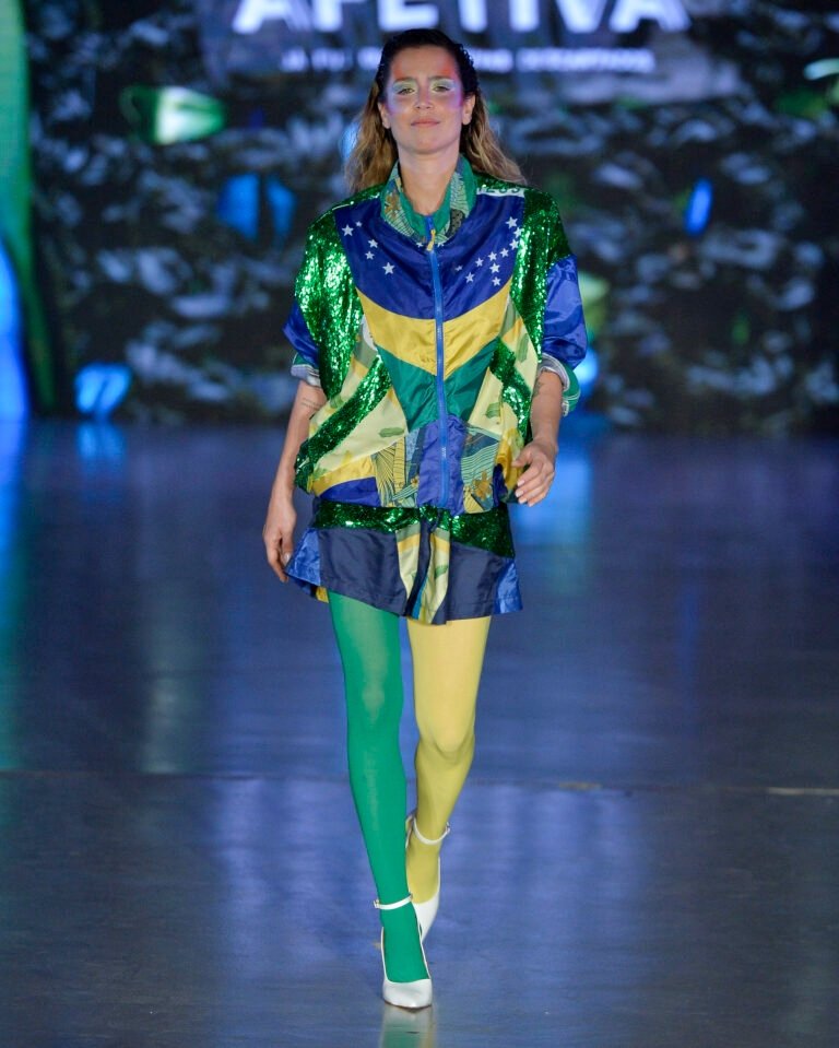 Modelo caminha com postura confiante na Casa de Criadores 57, usando jaqueta oversized e saia com paetês verdes, azul,