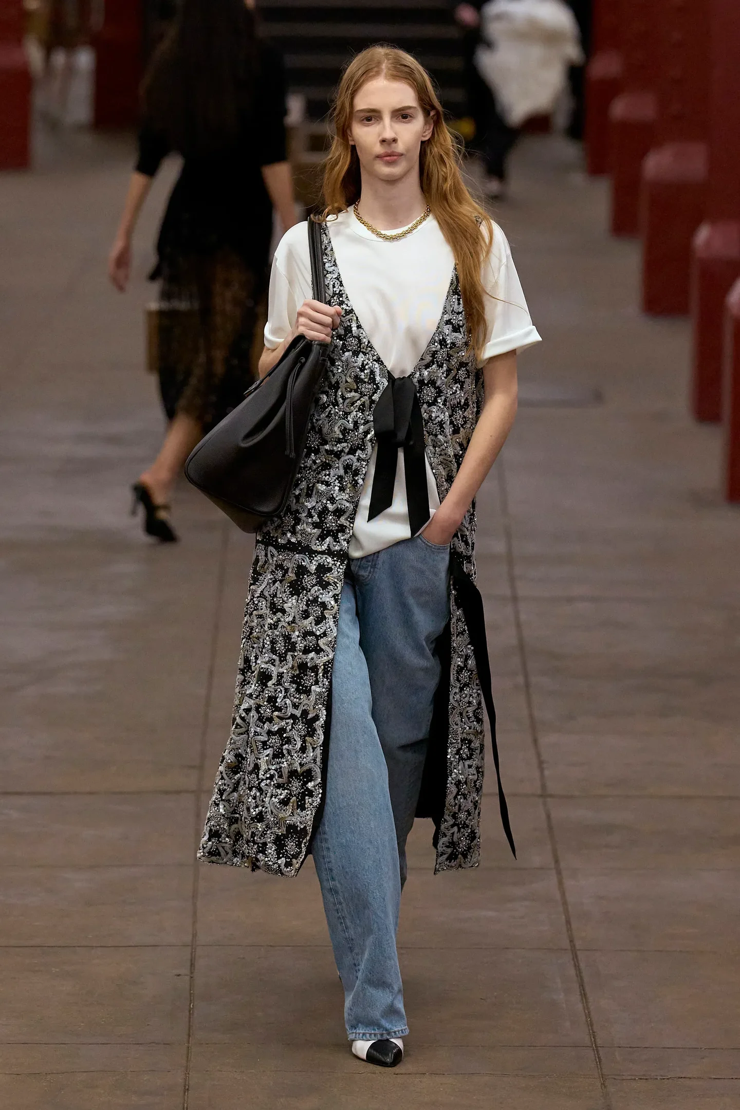 Modelo caminha com postura confiante na Chanel Métiers d’art 2026 usando colete bordado preto e branco sobre camiseta