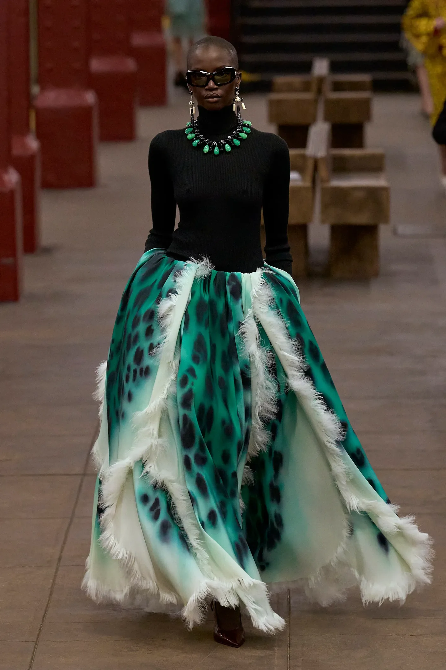 Modelo da Chanel Métiers d’art 2026 desfila com vestido de saia ampla verde com estampa animal e franjas brancas.