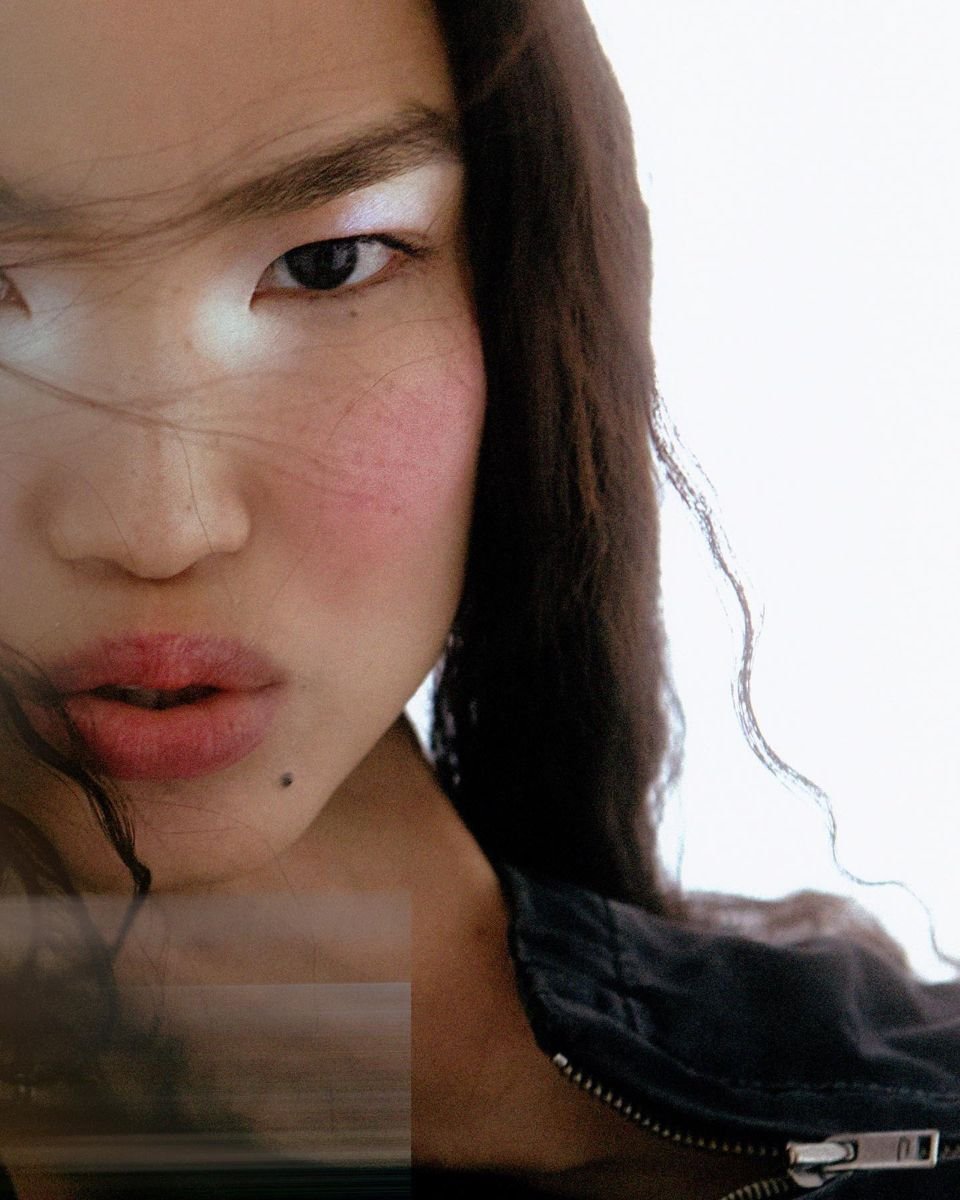 Modelo posa com expressão intensa e cabelos soltos, usando jaqueta preta de zíper que reforça o estilo urbano cloud dancer.