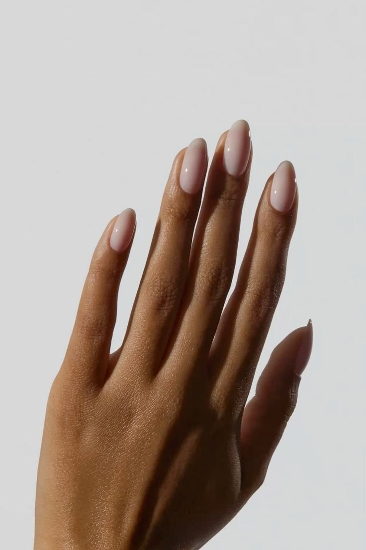 Unhas ovais com esmalte cloud dancer em tom nude rosado brilhoso destacam elegância e delicadeza minimalista.