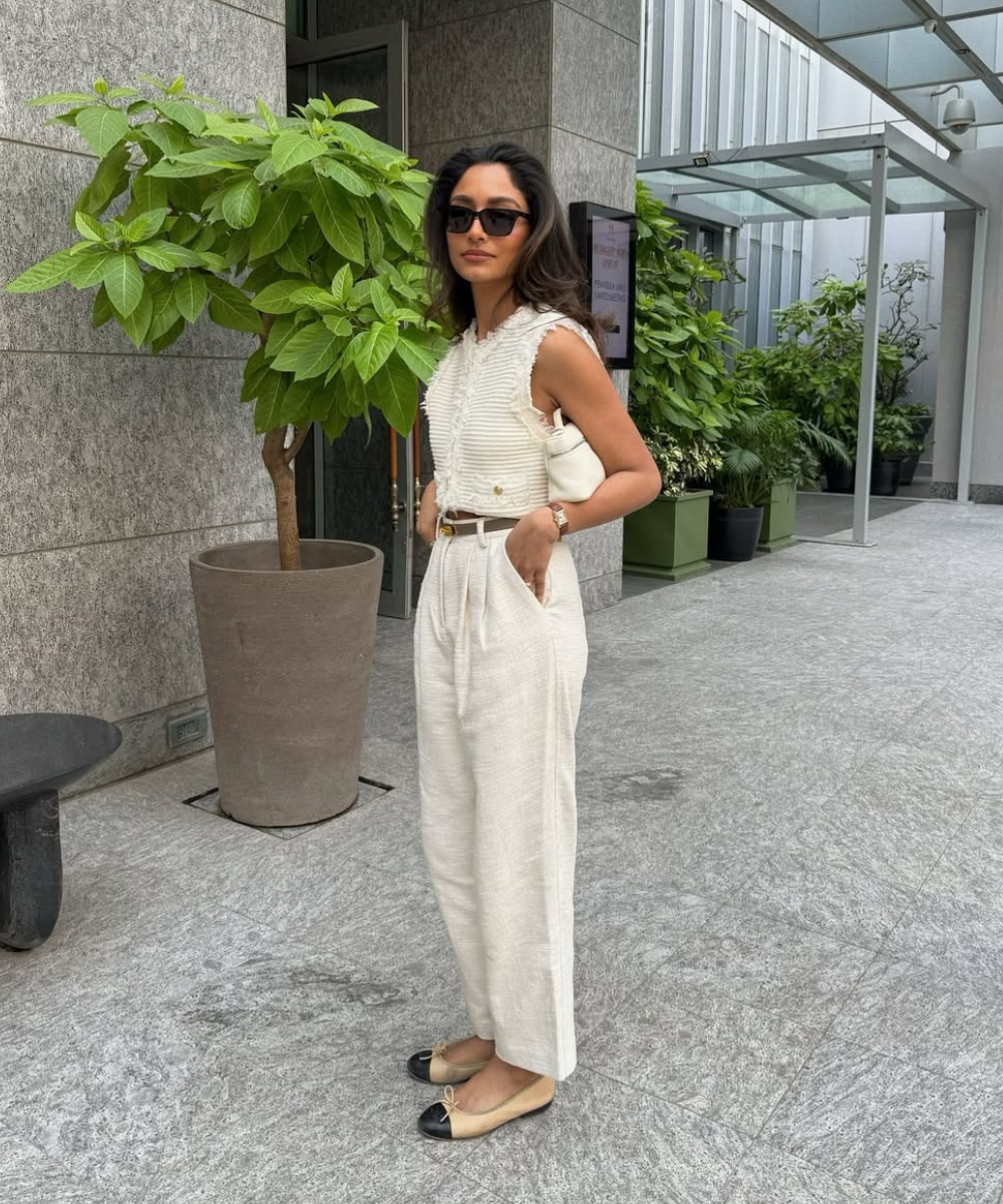 Modelo posa com colete texturizado e calça de linho off-white, combinando bolsa e sapatilha bicolor em ambiente urbano.