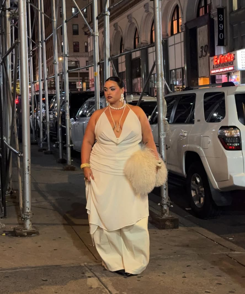 Modelo posa à noite com vestido fluido off-white de decote profundo, calça ampla, acessórios perolados e bolsa peluda.