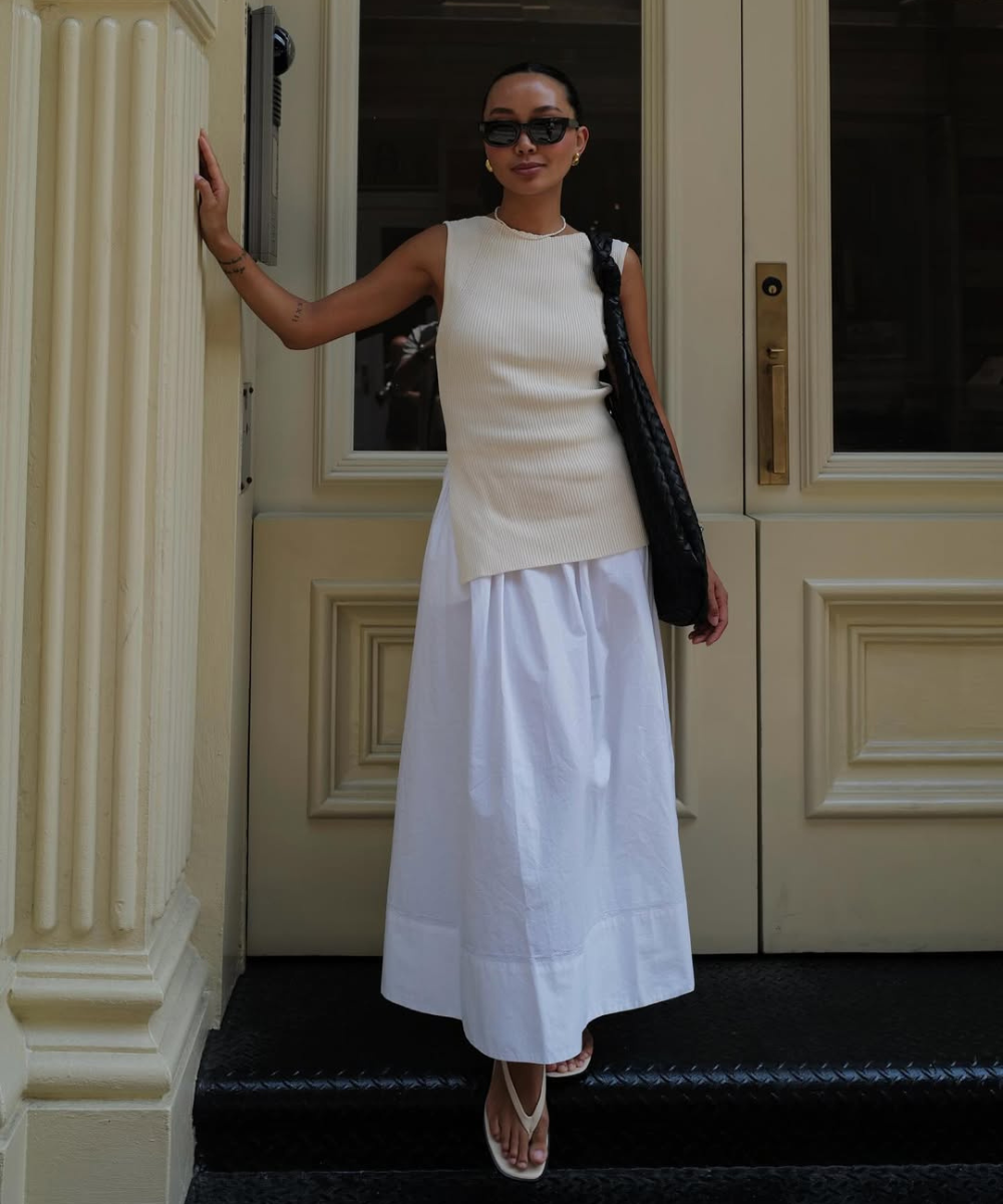 Modelo posa confiante com regata de tricô bege em modelagem alongada e saia branca ampla.
