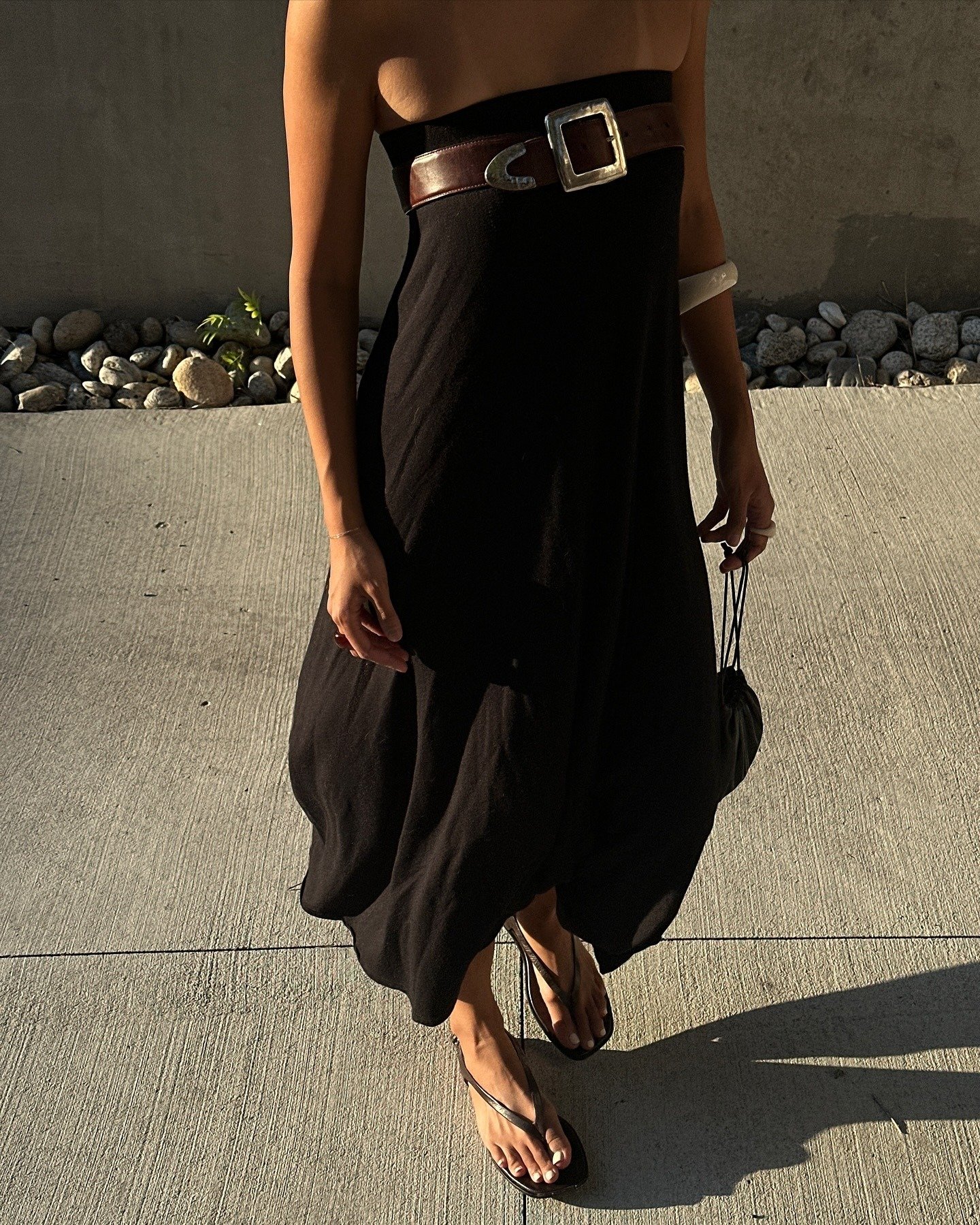 Modelo usa vestido preto de tecido fluido com cinto marrom de couro largo e fivela prateada, criando estilo sofisticado e