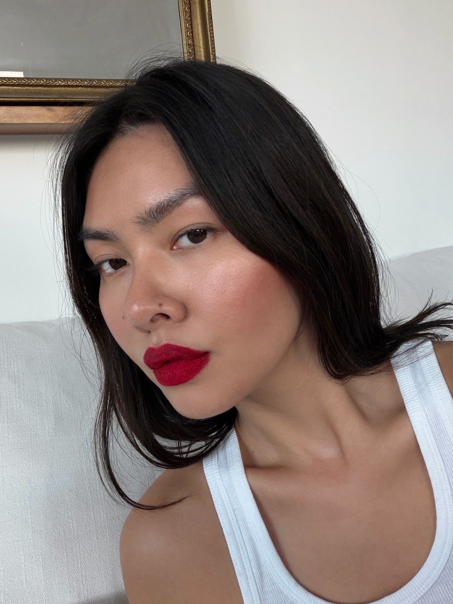 Modelo posa com batom vermelho vibrante, realçando a cor do ano 2026 em contraste com regata branca e pele natural iluminada.