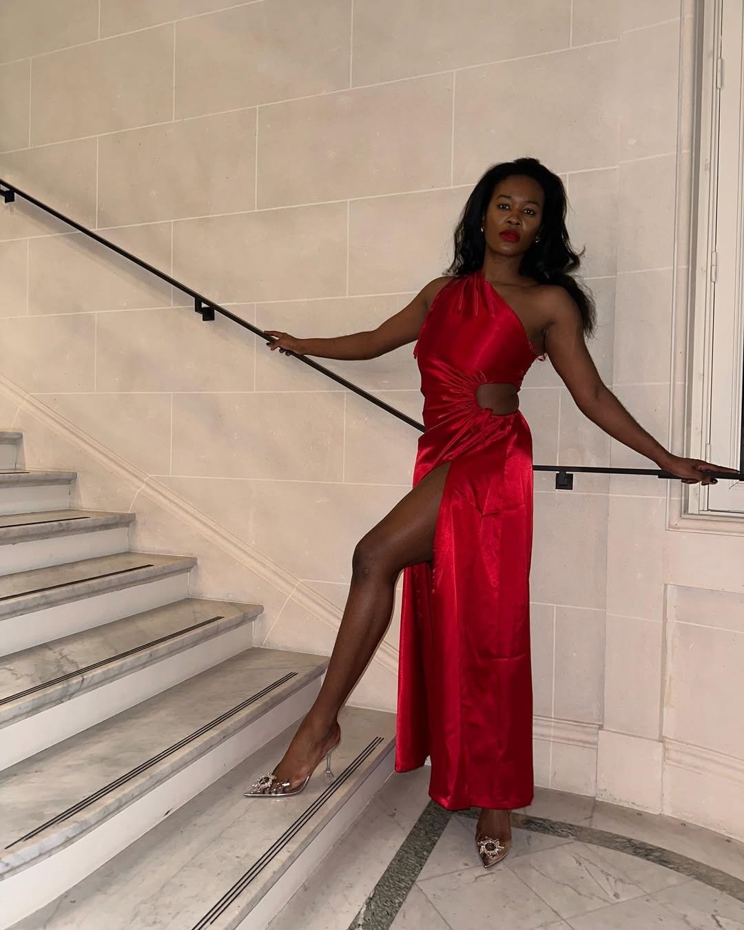 Modelo posa com vestido longo vermelho vibrante em cetim, recorte lateral e fenda alta, refletindo a cor do ano 2026