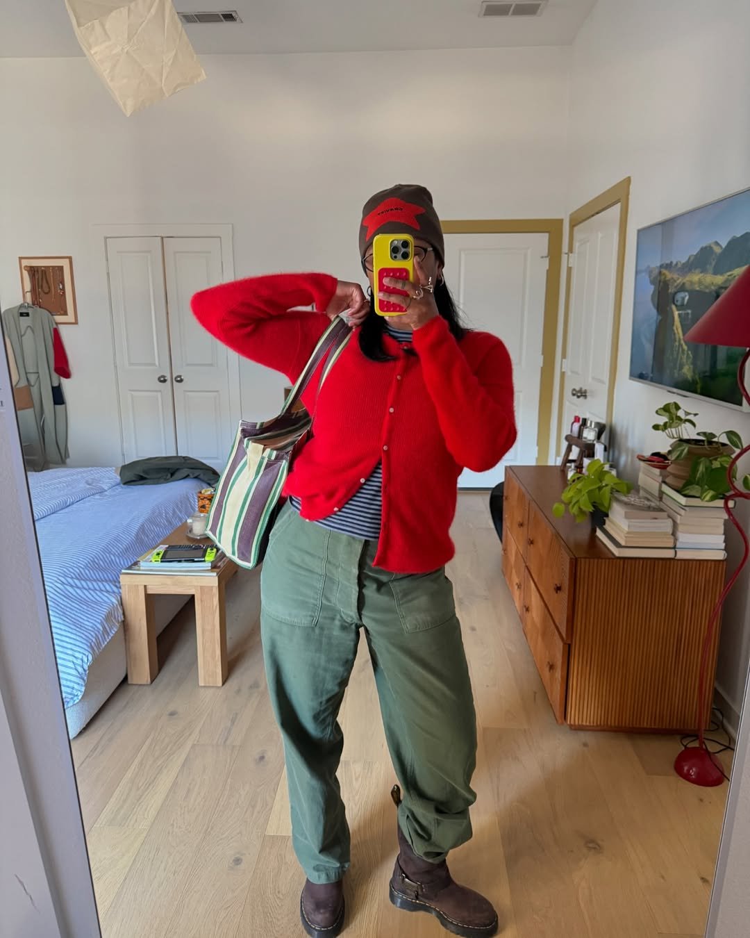 Mulher usa look verde e vermelho, cores de Capricórnio para 2026, posando em frente ao espelho de quarto decorado com livros