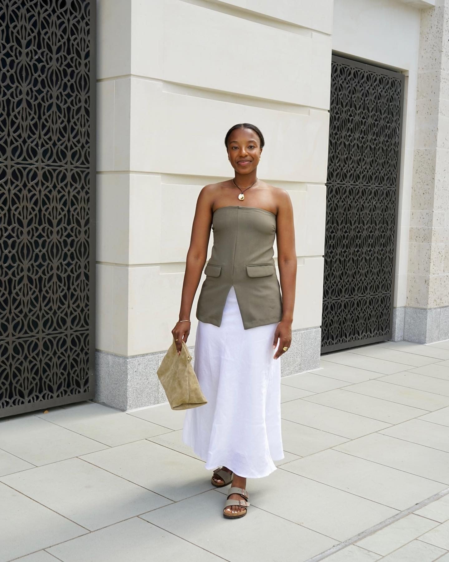 Mulher caminha confiante com papete bege de tiras largas, combinando com saia branca fluida e top tomara que caia