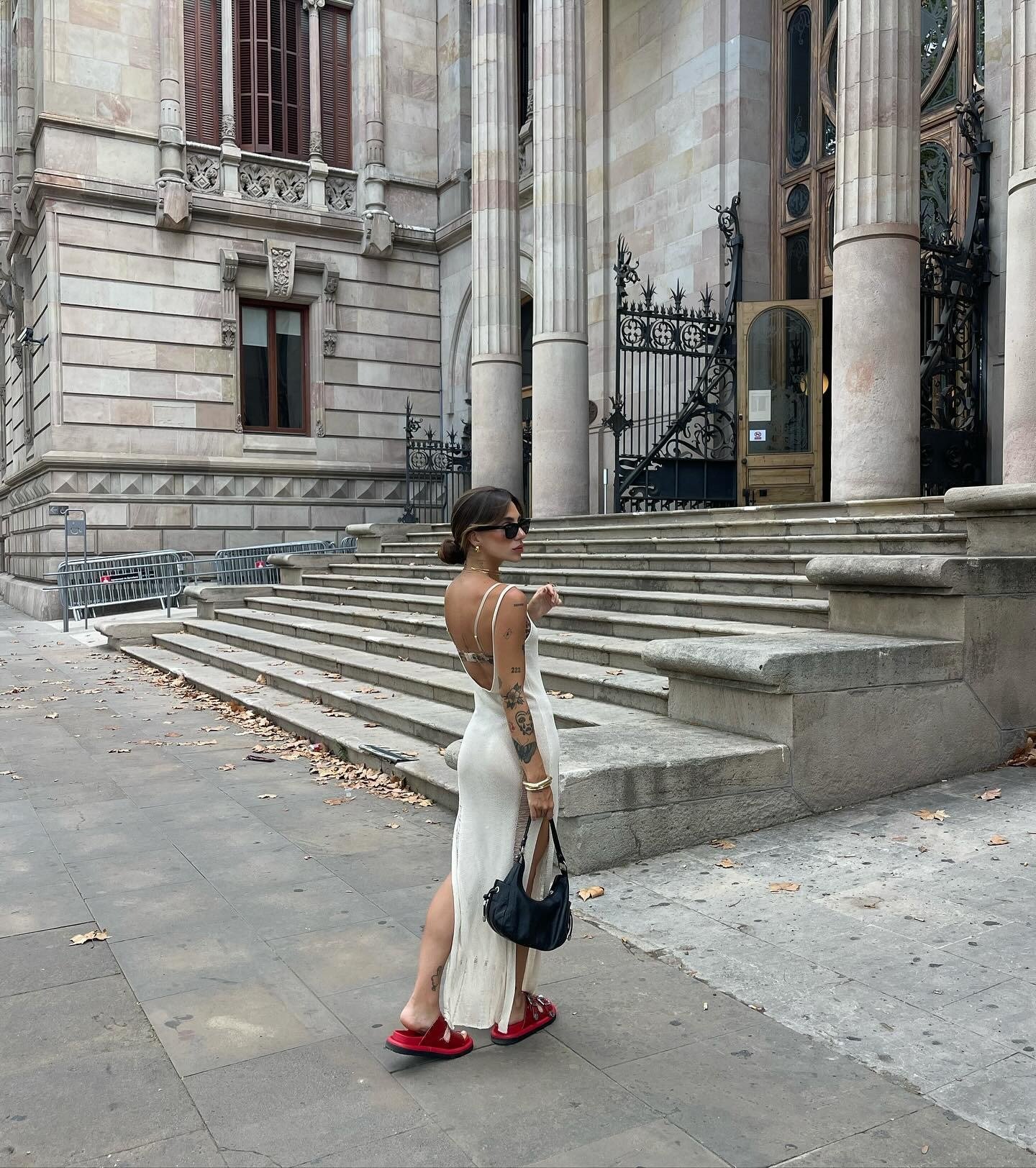 Mulher posa de costas com vestido branco longo de malha e papete vermelha, combinando estilo casual e urbano com toque