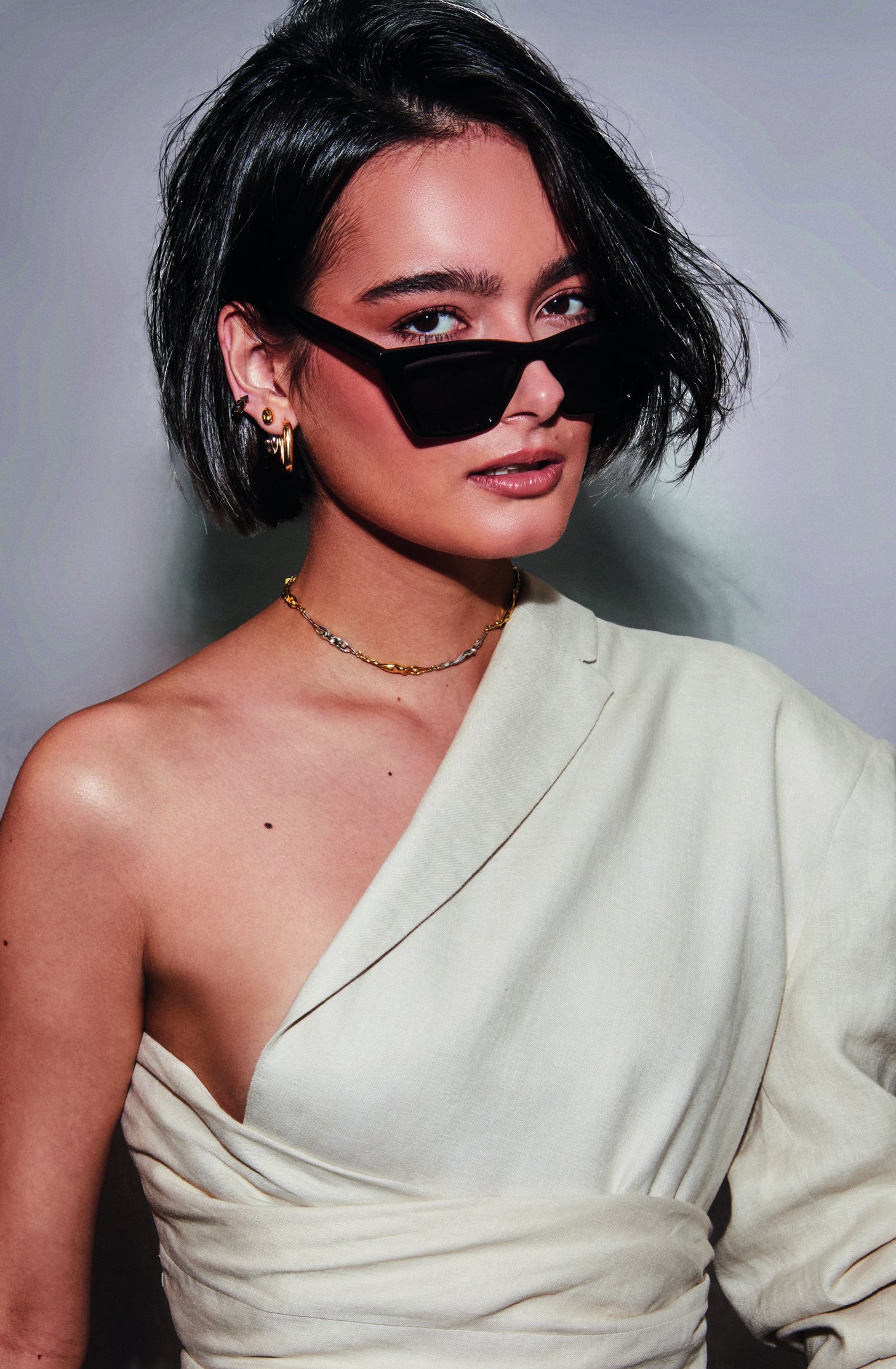 Modelo posa com cortes de cabelo da moda em bob assimétrico preto, combinando óculos escuros quadrados e look off-white