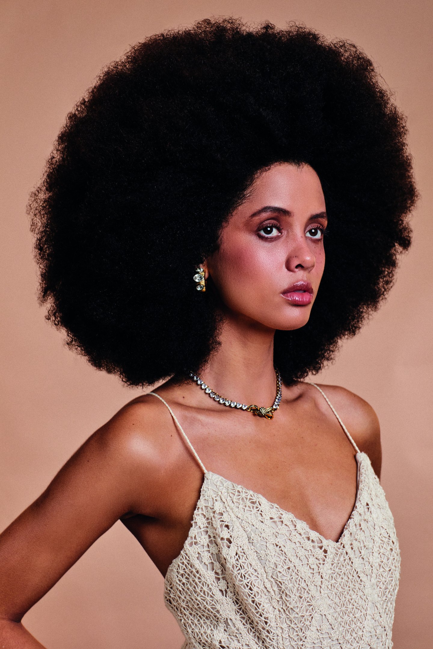 Modelo posa com cortes de cabelo da moda em bob assimétrico preto, combinando blazer off-white e acessórios dourados