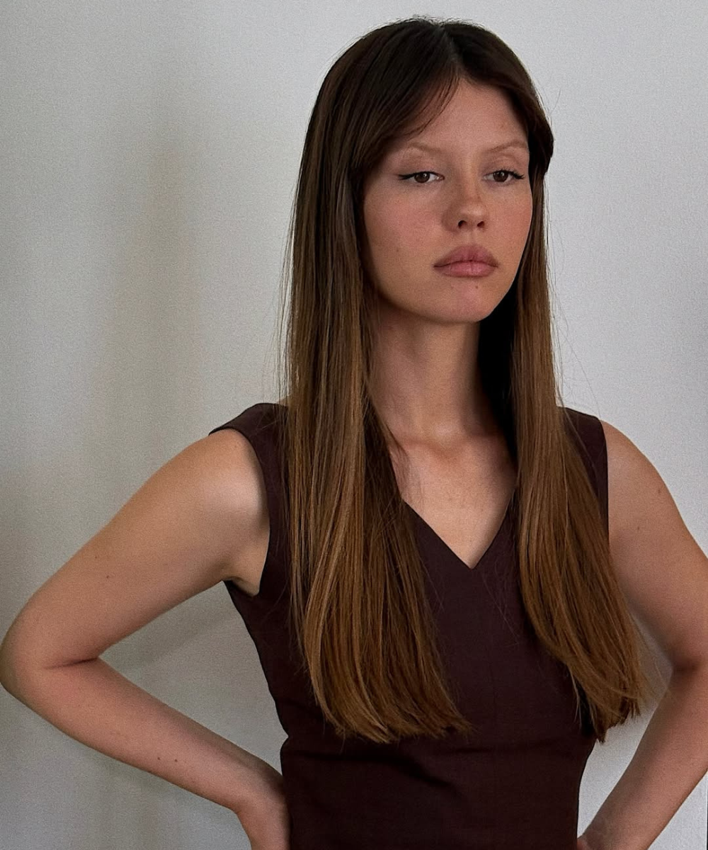 Modelo posa com corte de cabelo das celebridades longo, liso e com franja central, vestindo blusa marrom.