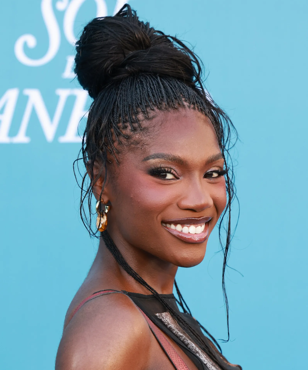 Cortes de cabelo das celebridades destacam tranças finas presas em coque alto, com fios soltos, realçando sorriso radiante.