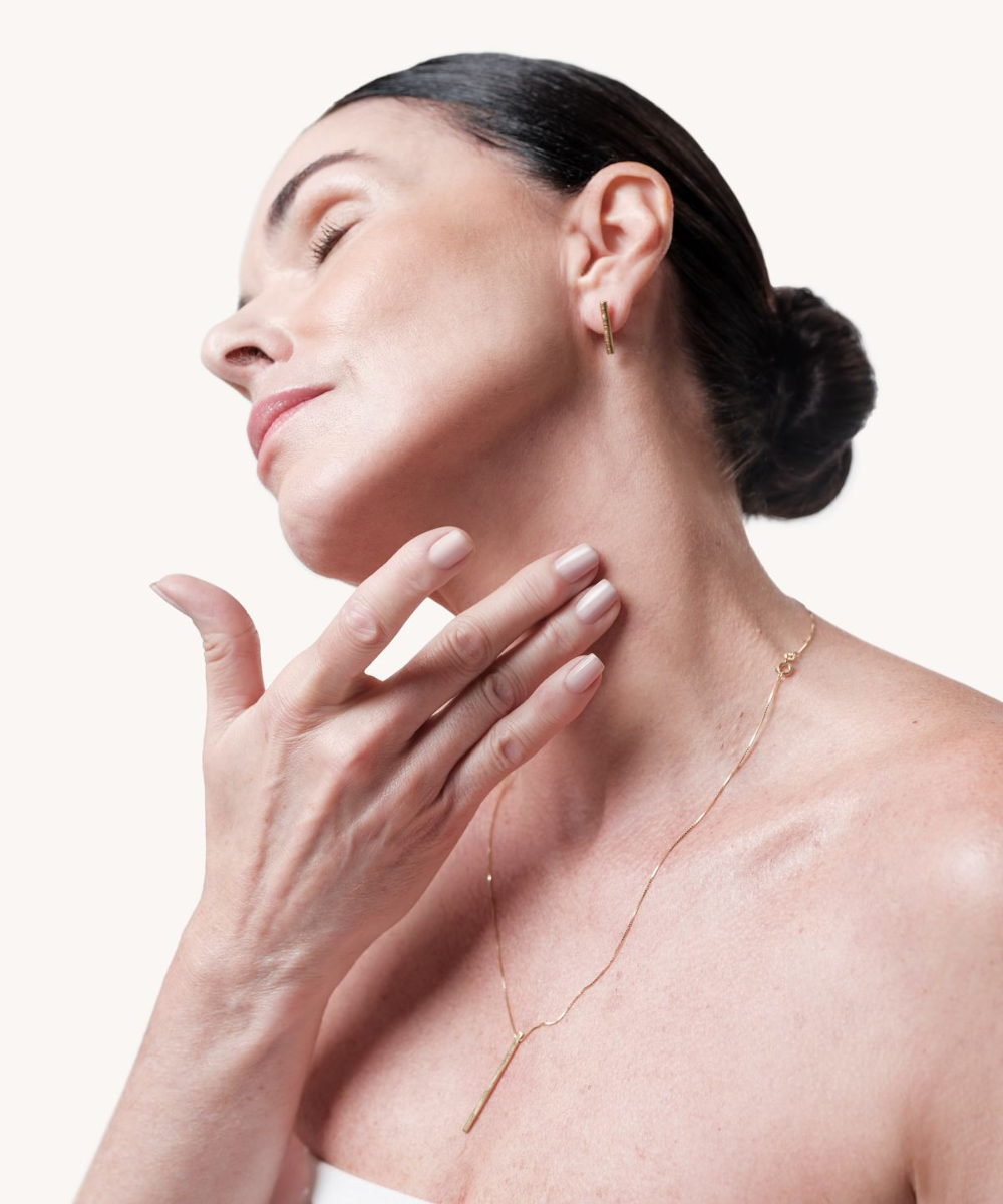 Mulher com cabelo preso toca o pescoço em gesto suave, destacando a importância de cuidar da pele do colo e do pescoço.