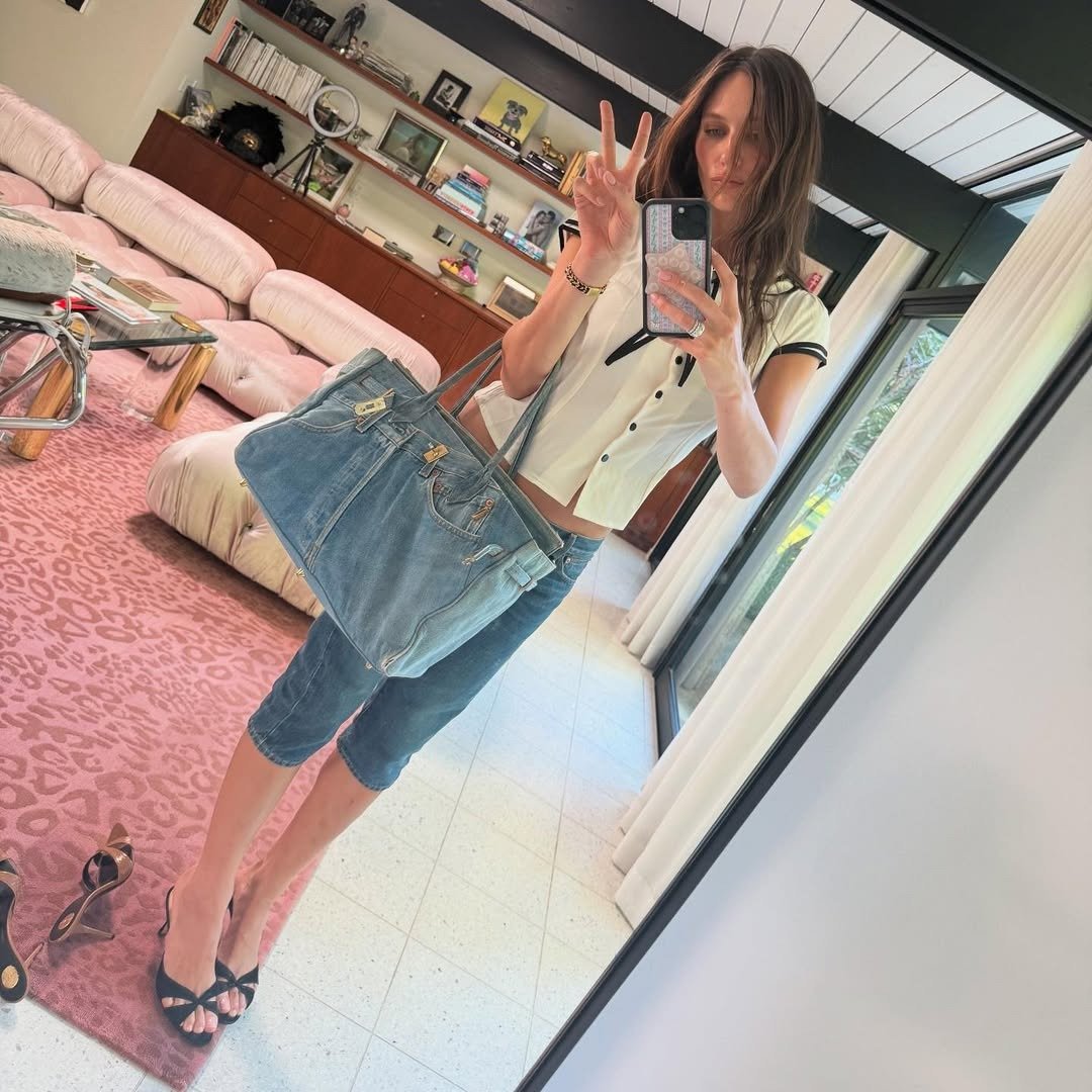 Devon Lee Carlson posa com estilo casual e despojado usando blusa cropped branca com detalhes pretos, bermuda jeans justa e