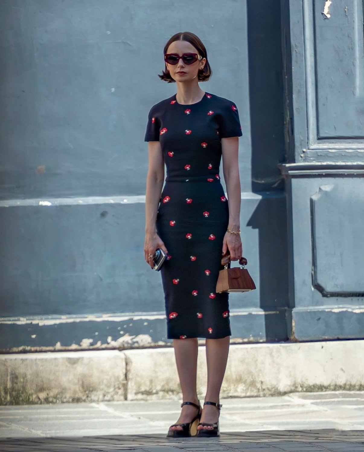 Emily em Paris exibe vestido midi justo preto com estampa de flores vermelhas, sandálias plataforma e bolsa marrom