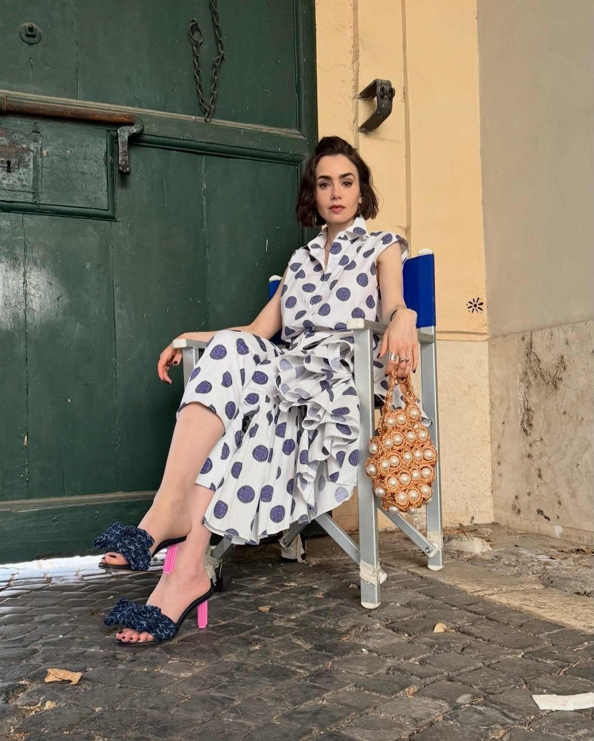 Emily em Paris exibe vestido branco com bolinhas azuis, modelagem fluida e babados, combinando sandálias de salto rosa