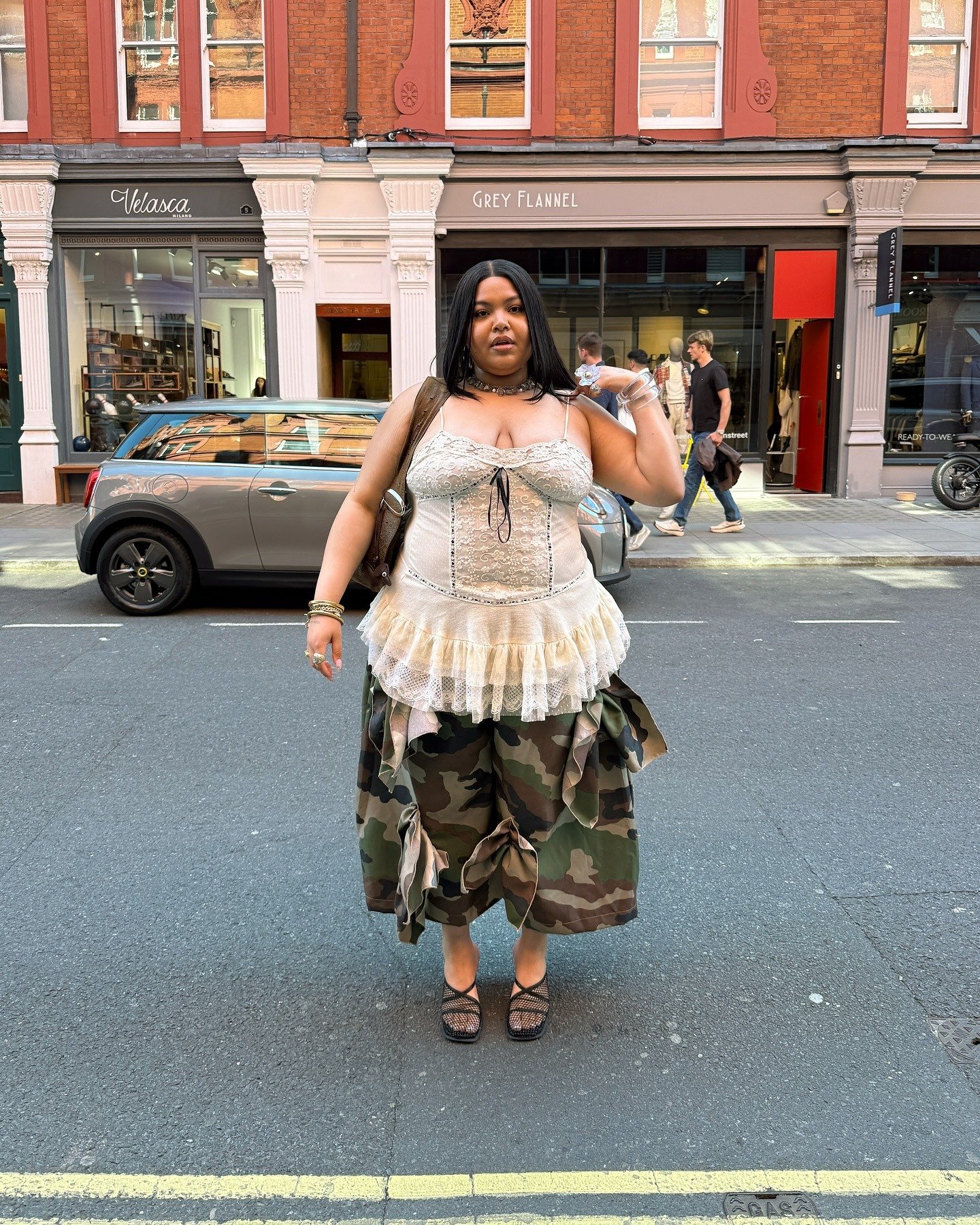 Modelo posa confiante com top corset de renda e babados em tons neutros combinado a saia camuflada oversized