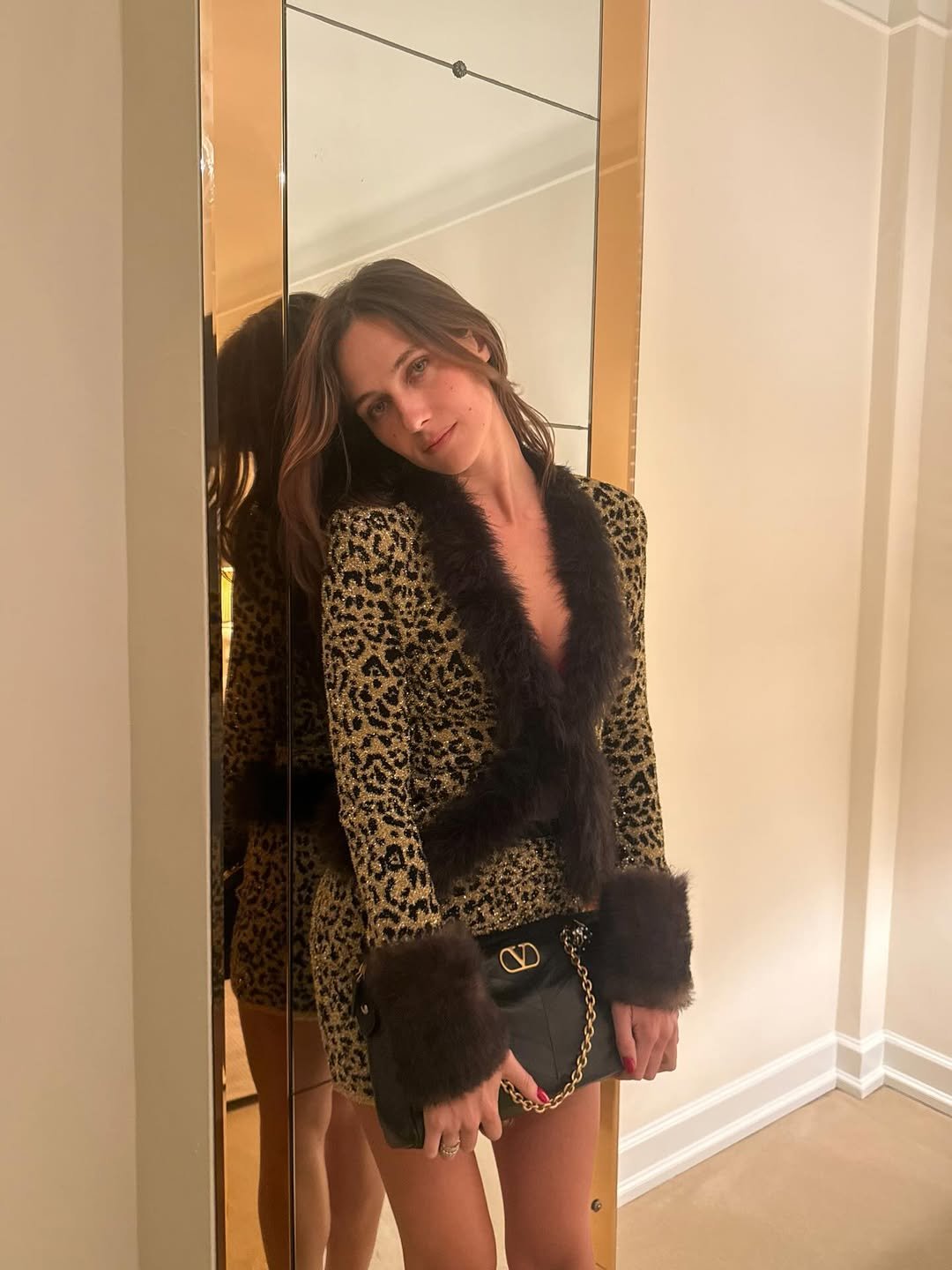 Devon Lee Carlson exibe estilo com vestido curto animal print em tecido brilhante, detalhes em pelúcia preta e clutch preta