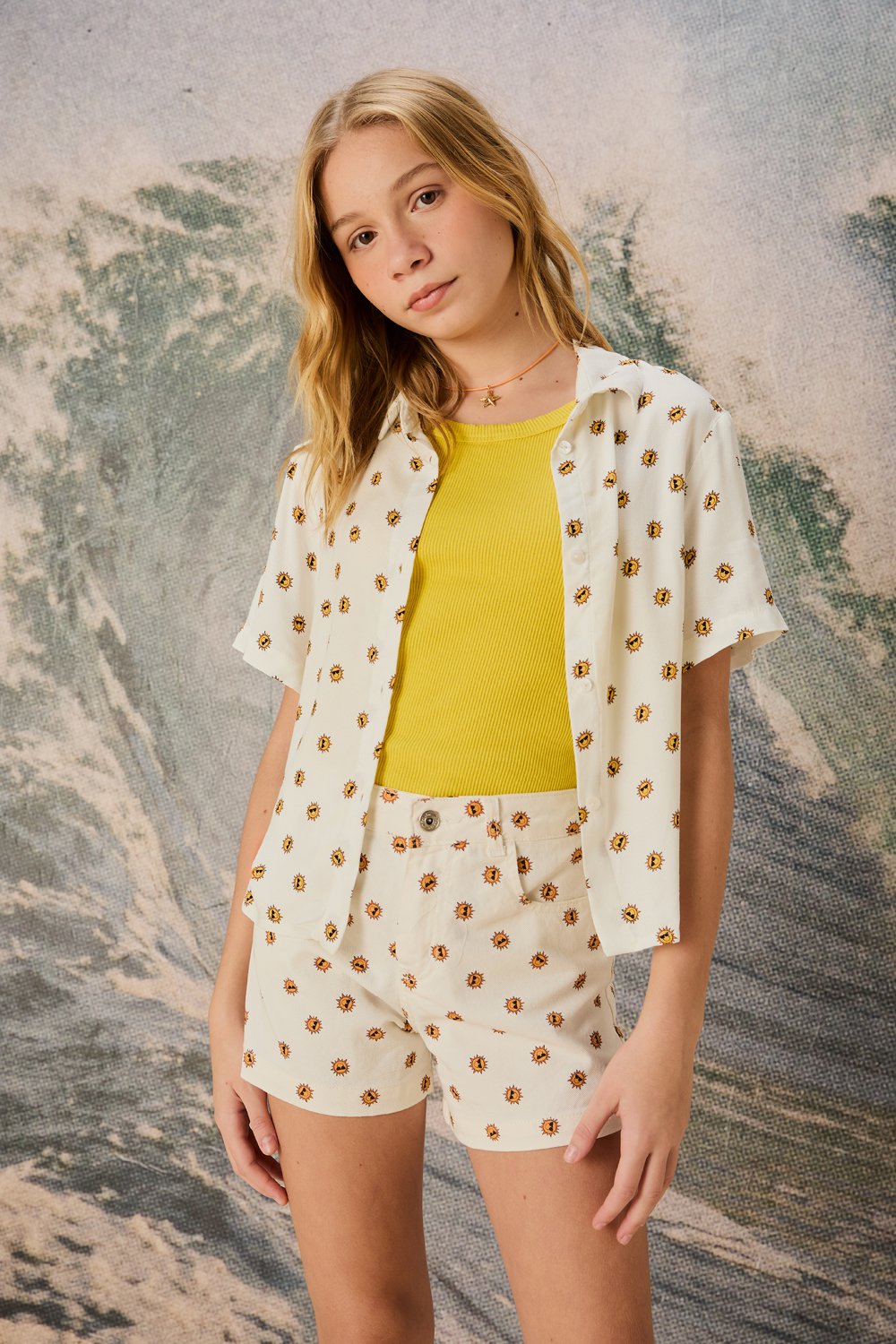Modelo posa com camisa e shorts de algodão off-white estampados por pequenos sóis amarelos e laranja, combinados com regata