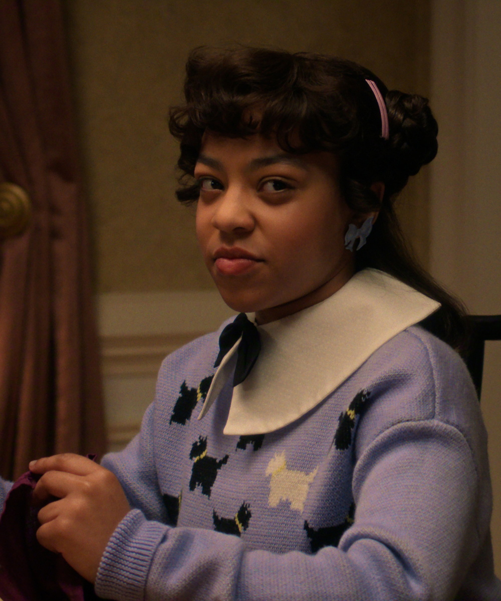 Personagem de Stranger Things usa suéter lilás com estampa de cachorros, gola branca ampla e laço preto.