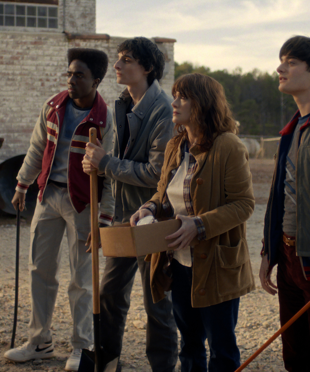 Personagens de Stranger Things vestem jaquetas e camisas em tons terrosos e neutros, com modelagens retrô e postura atenta