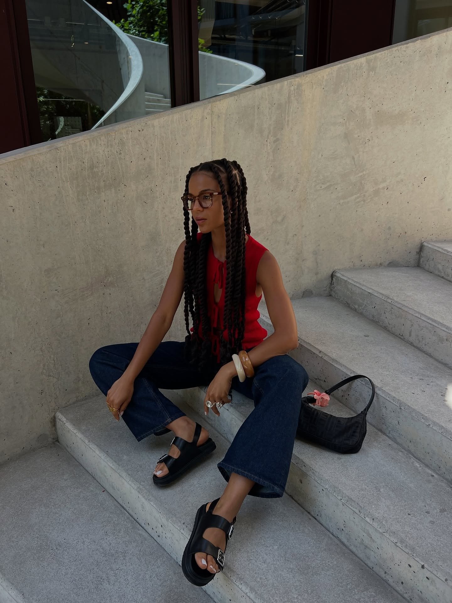 Modelo senta nas escadas com blusa vermelha de tricô, jeans flare escuro e flatform preto de tiras largas, em clima urbano