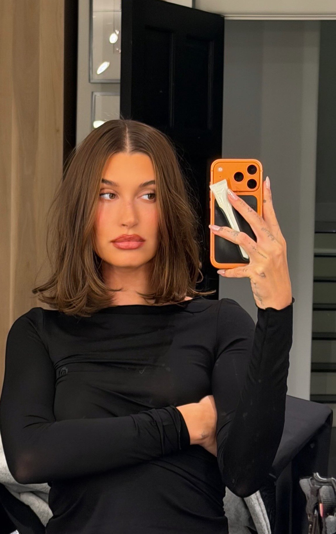 Hailey Bieber posa para selfie com cabelo médio castanho, liso com pontas levemente onduladas. Novo cabelo da Hailey Bieber