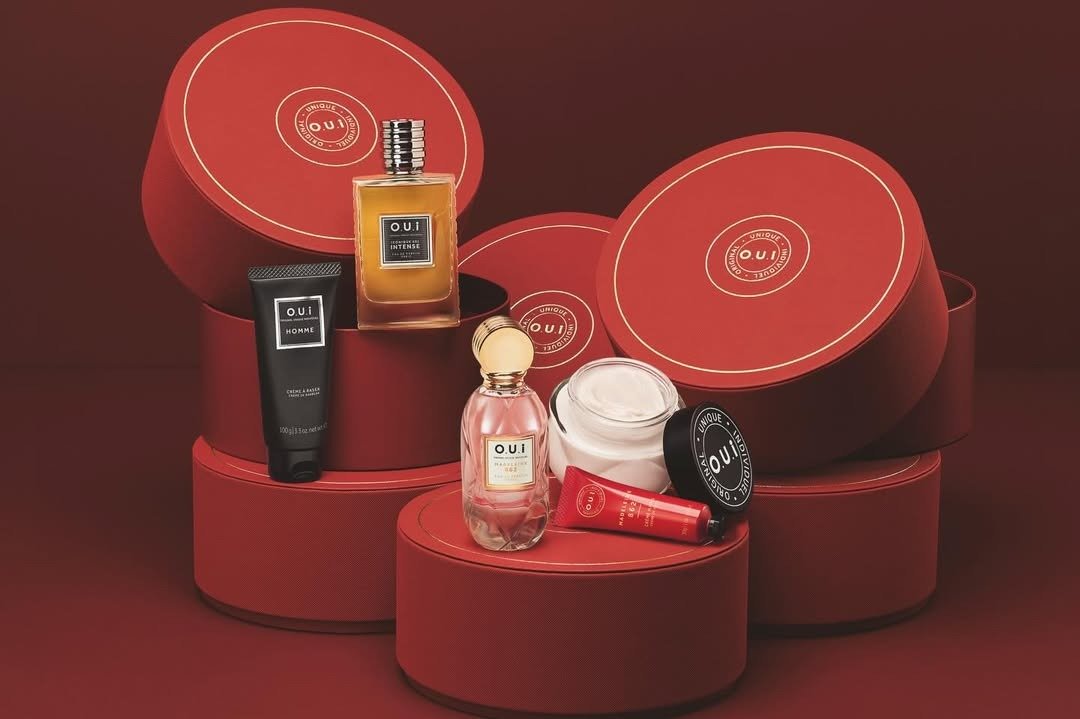 Kits de fragrâncias de Natal exibem embalagens redondas vermelhas com perfumes e cremes em vidro e plástico, sugerindo luxo