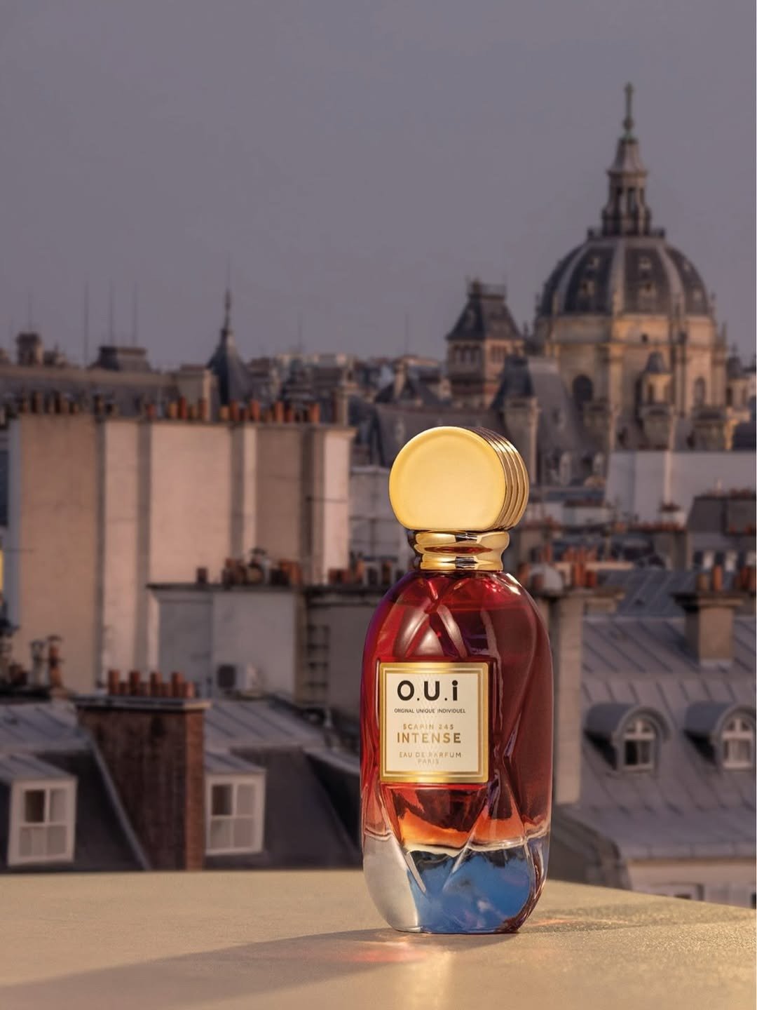 Frasco luxuoso em vidro translúcido vermelho com tampa dourada destaca kits de fragrâncias de Natal em cenário urbano