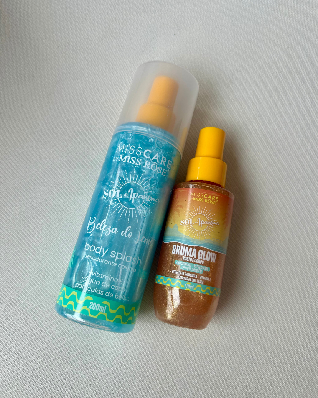 Frascos spray azul e bronze com tampa amarela da linha de hidratante firmador, sugerindo frescor e brilho