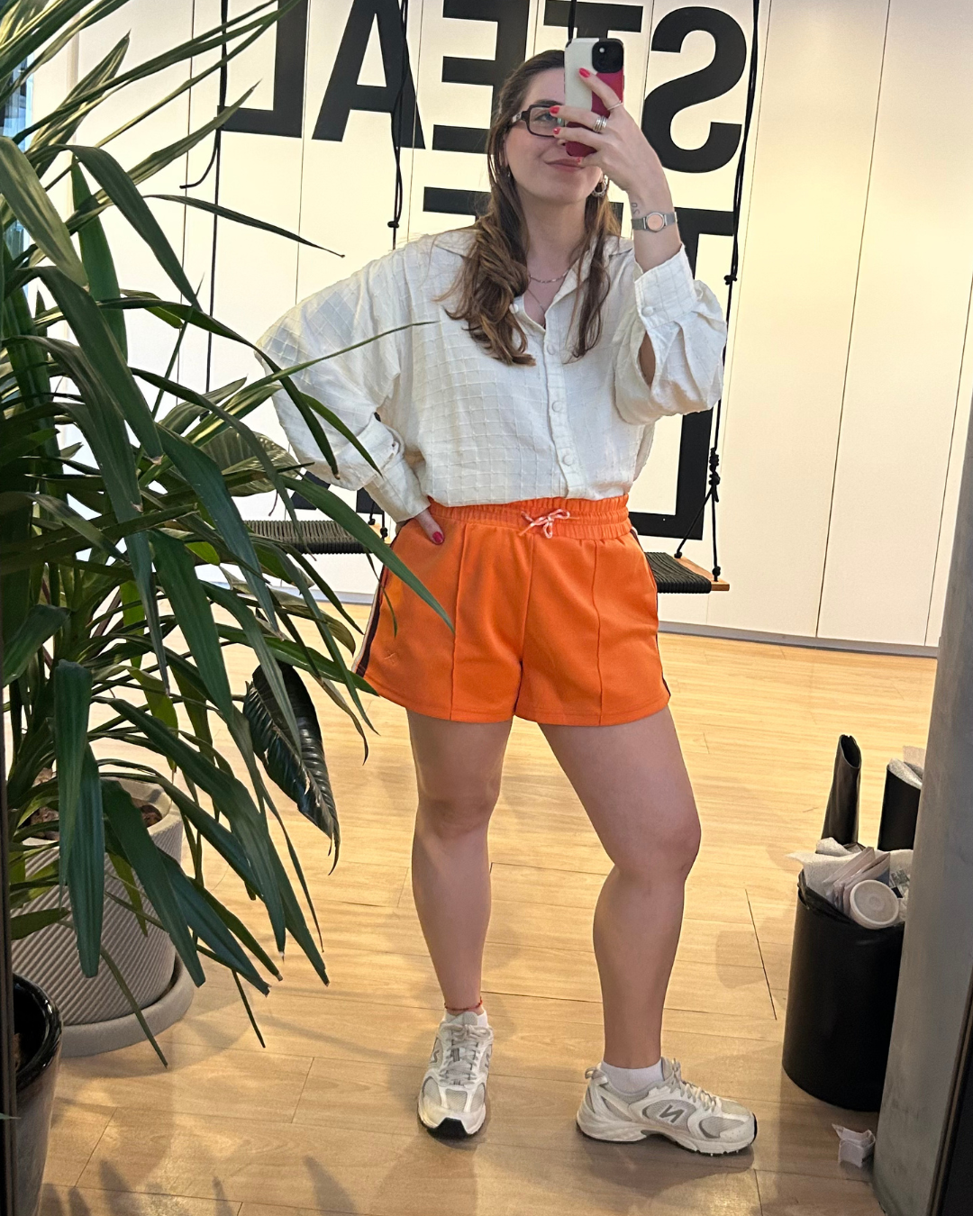 Mulher posa com camisa branca texturizada e shorts laranja e pernas depois do creme texturizador 