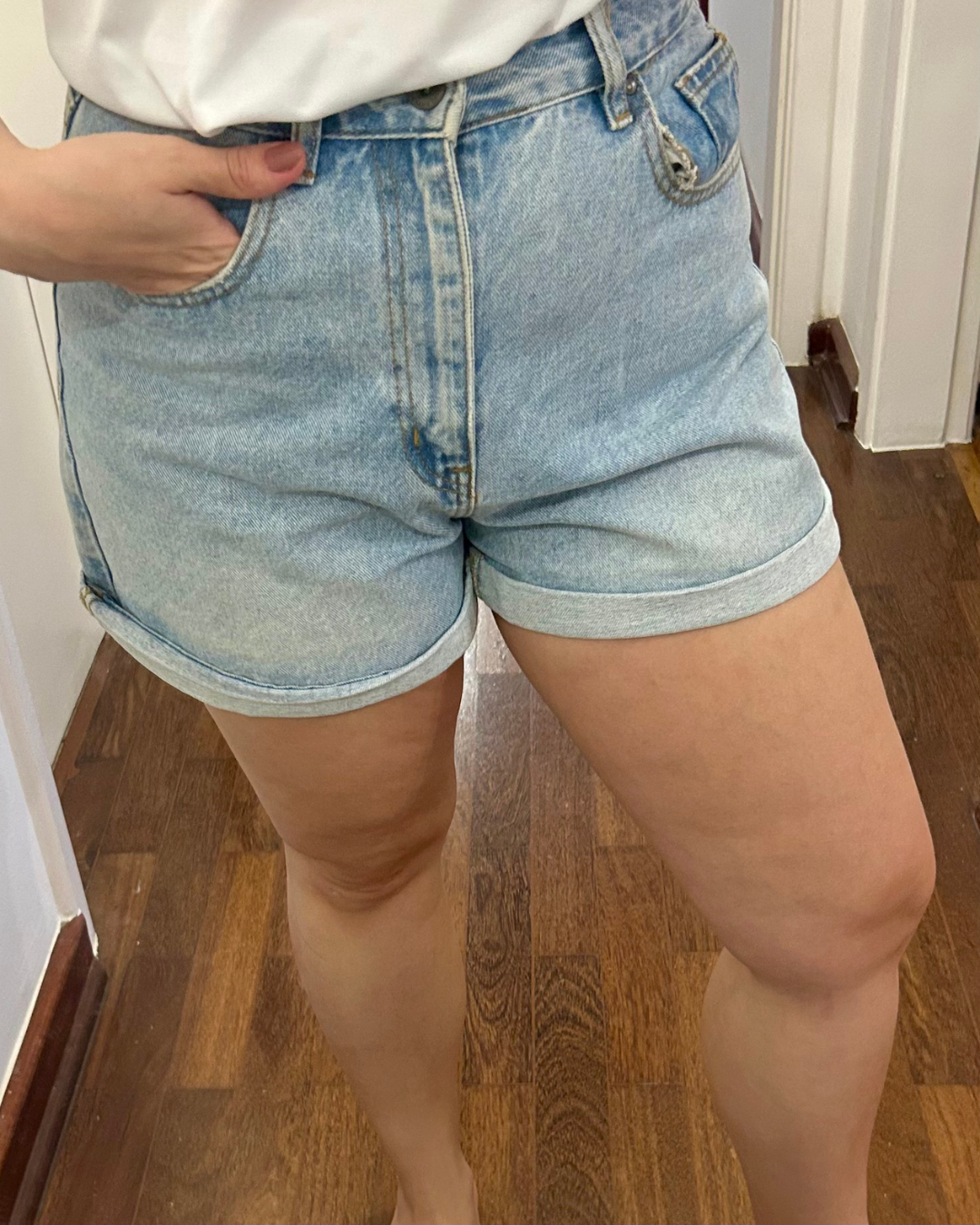 Modelo posa com shorts jeans claro de barra dobrada e blusa branca, destacando pele firme e natural de creme firmador