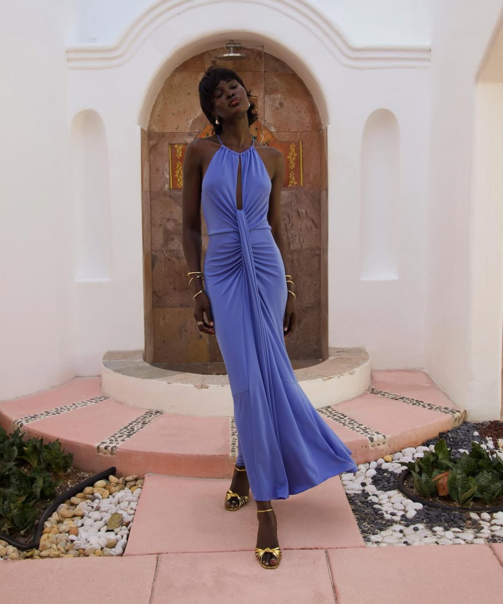 Vestido azul lavanda longo com decote halter e drapeado frontal em tecido fluido, modelo posa com elegância e atitude serena.