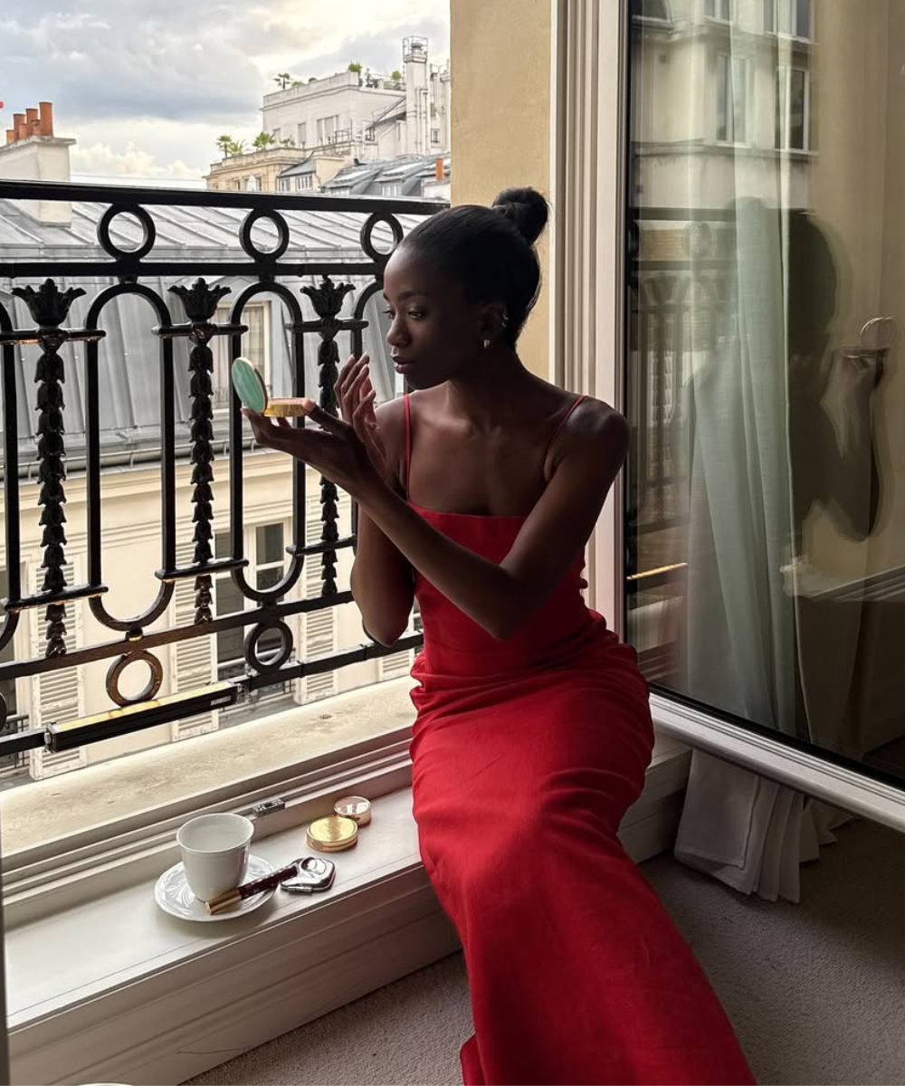 Modelo senta à janela em vestido longo vermelho de alças finas e tecido fluido, criando looks bonitos com vestidos elegantes