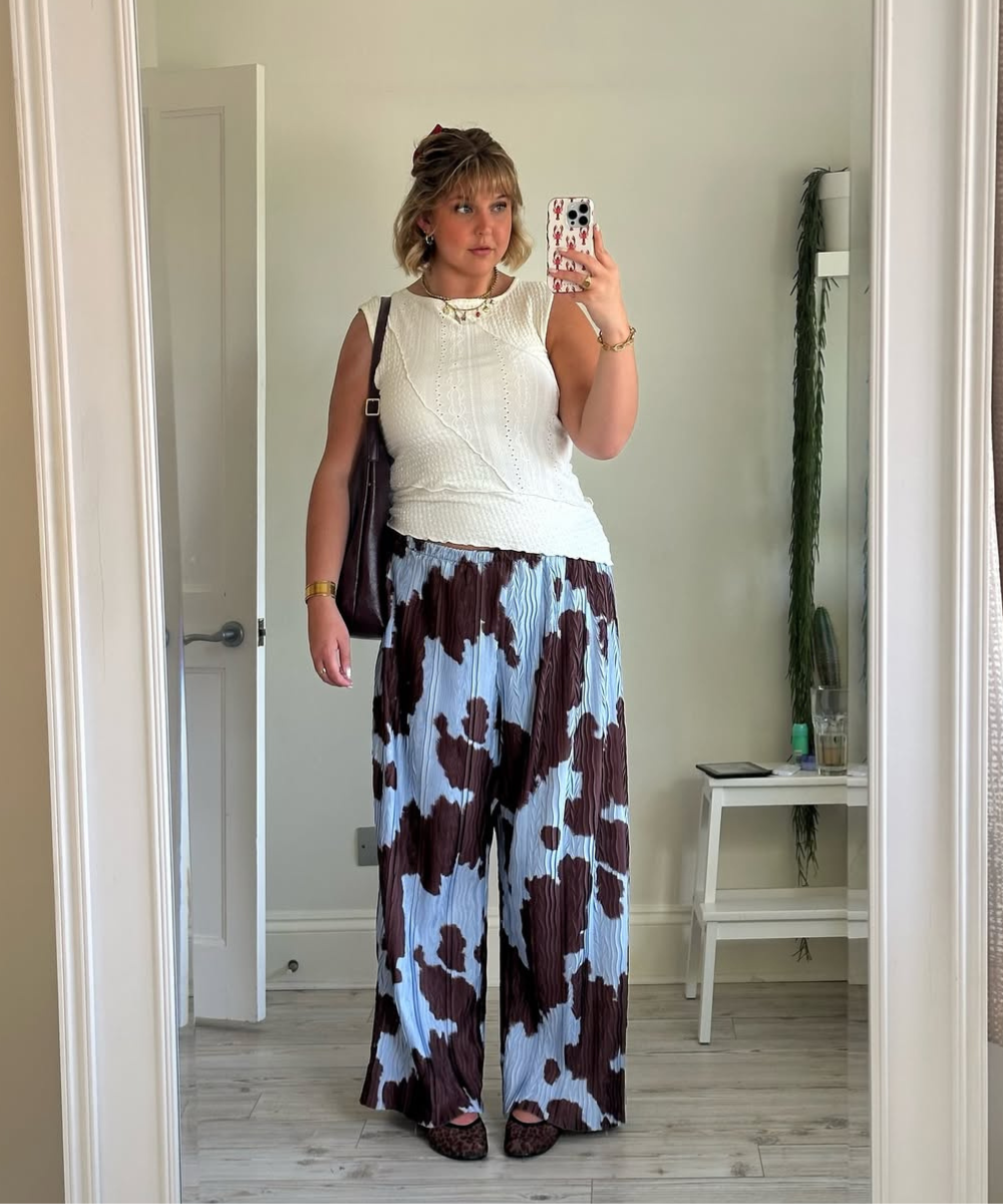 Modelo posa em frente ao espelho com blusa branca texturizada sem mangas e calça pantalona plissada azul clara com estampa