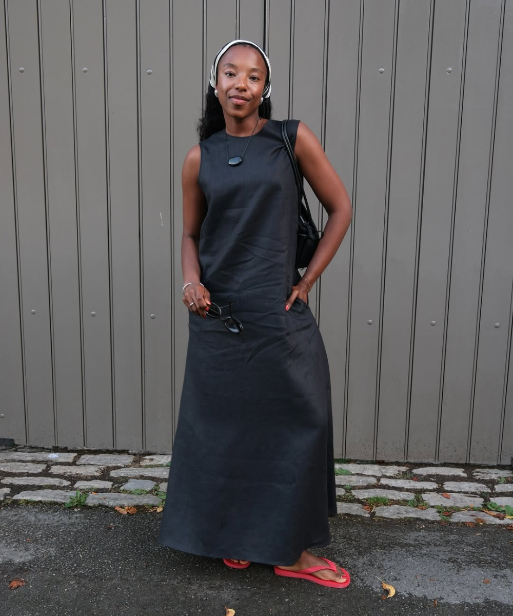 Modelo posa com vestido longo preto de tecido liso, sandálias vermelhas, lenço branco na cabeça e acessórios minimalistas.