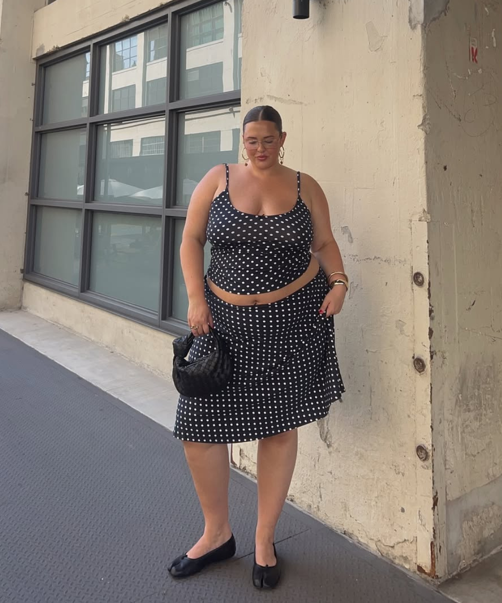 Modelo posa usando conjunto preto de poás brancos em tecido leve, bolsa pequena preta e sapatilhas.