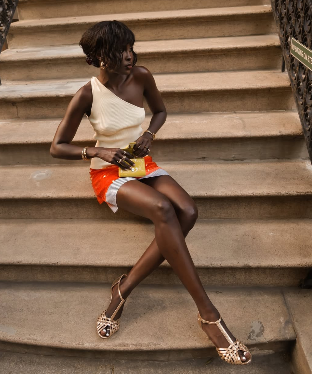 Mulher sentada em uma escada. Usa saia de paetê com ombro de fora e sandália. Inspiração de looks chiques para festas.