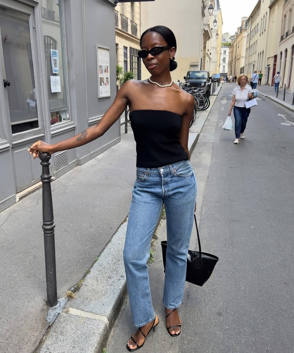 Look com calça justa jeans reta, top tomara que caia preto e sandálias de tiras finas, estilo urbano sofisticado e confiante.