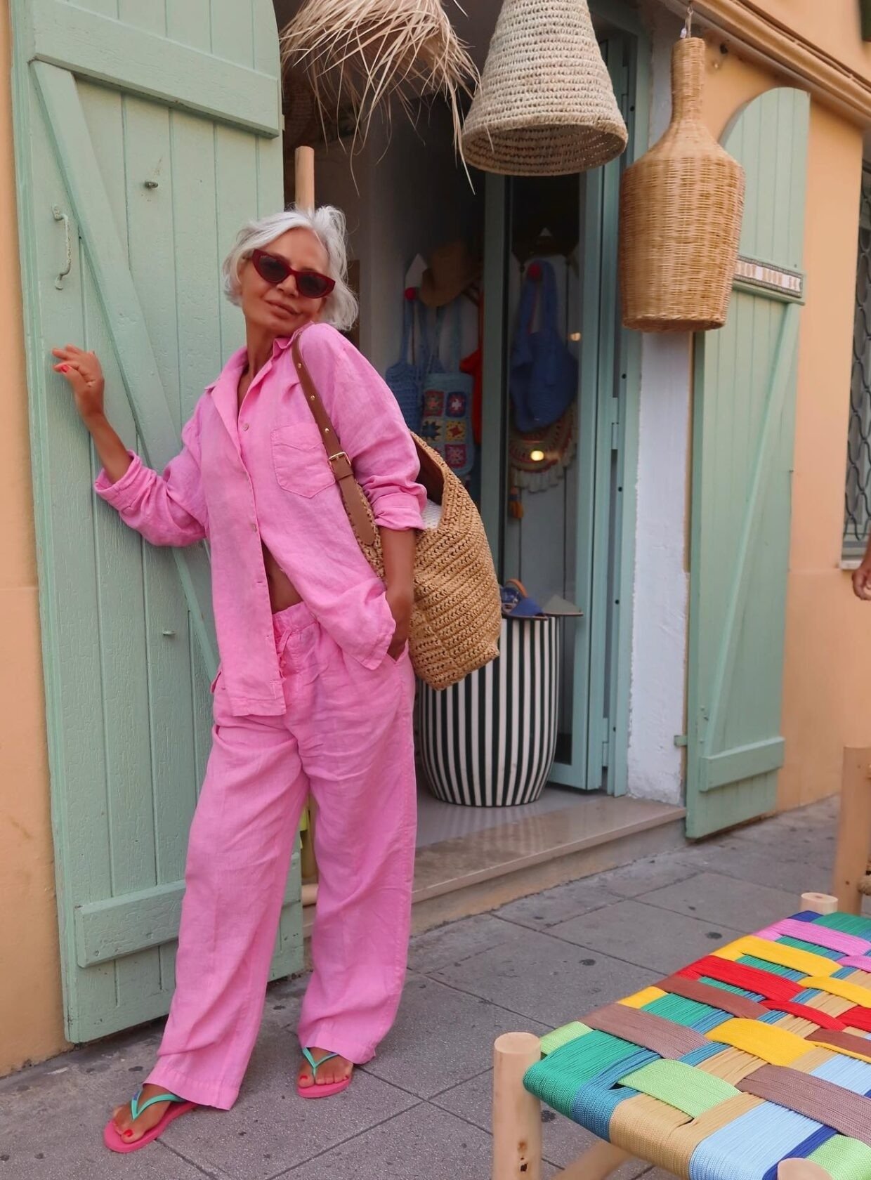 Mulher posa com conjunto rosa de linho solto e chinelo rosa com tiras azul, em clima descontraído e verão urbano.