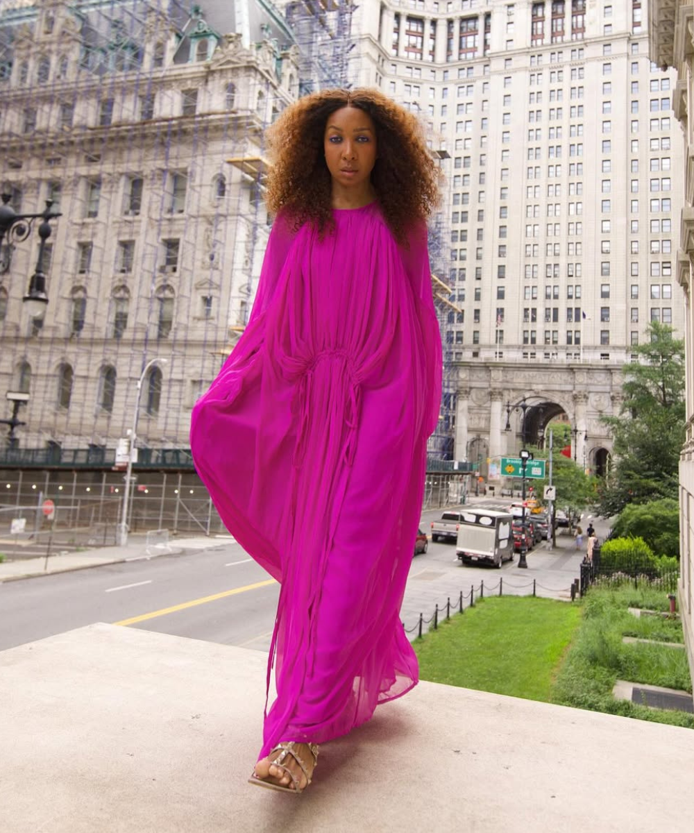 Modelo caminha com postura confiante usando vestido fluido rosa vibrante e sandália gladiadora bege com tiras finas.