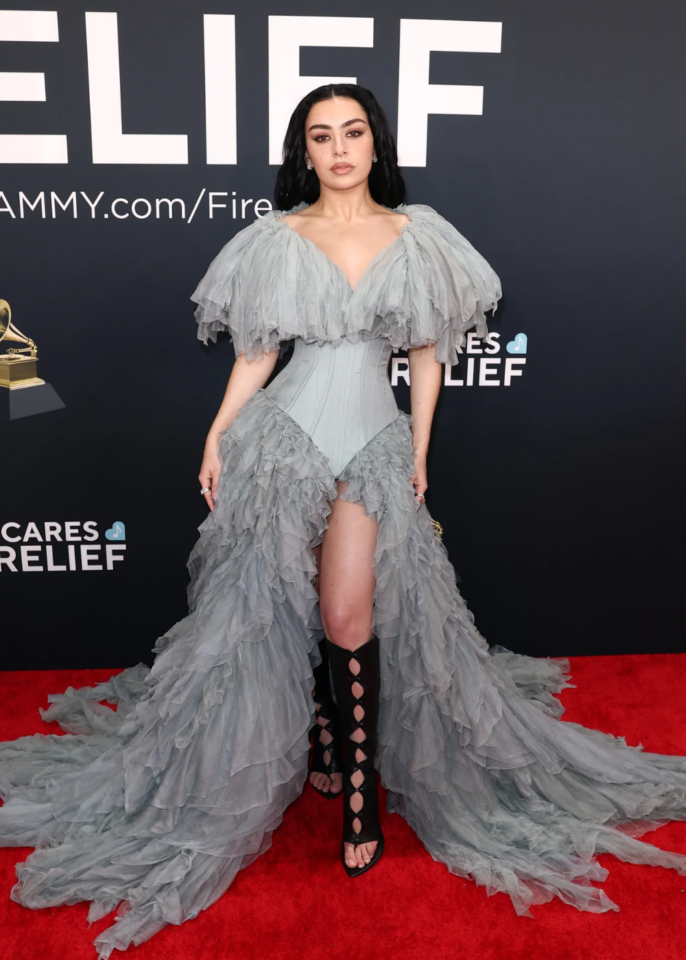 Modelo posa com vestido cinza de tule volumoso e corset estruturado, combinando sandália gladiadora preta de tiras.