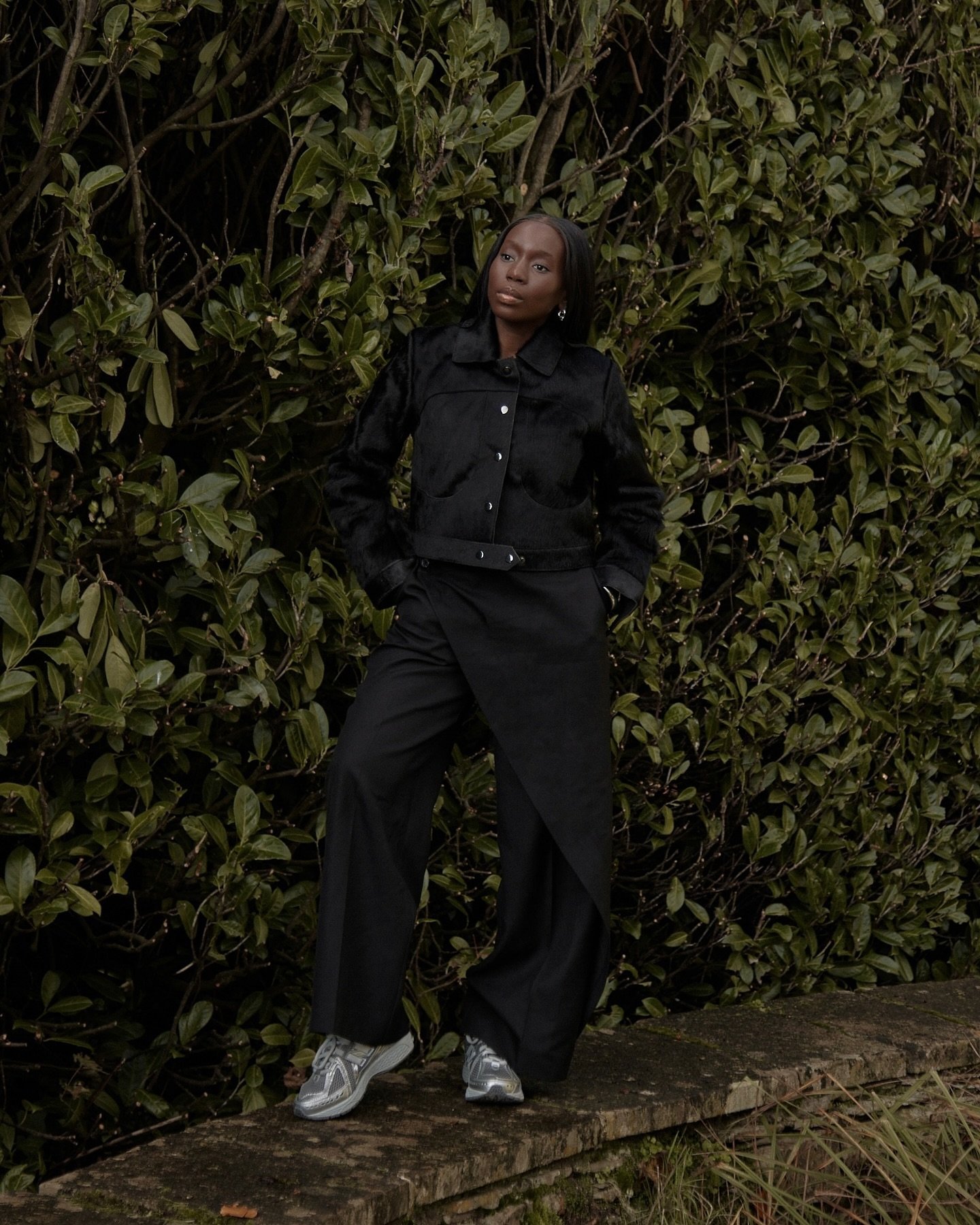 Modelo posa com postura confiante usando jaqueta cropped preta de textura aveludada, calça preta ampla com sobreposição e