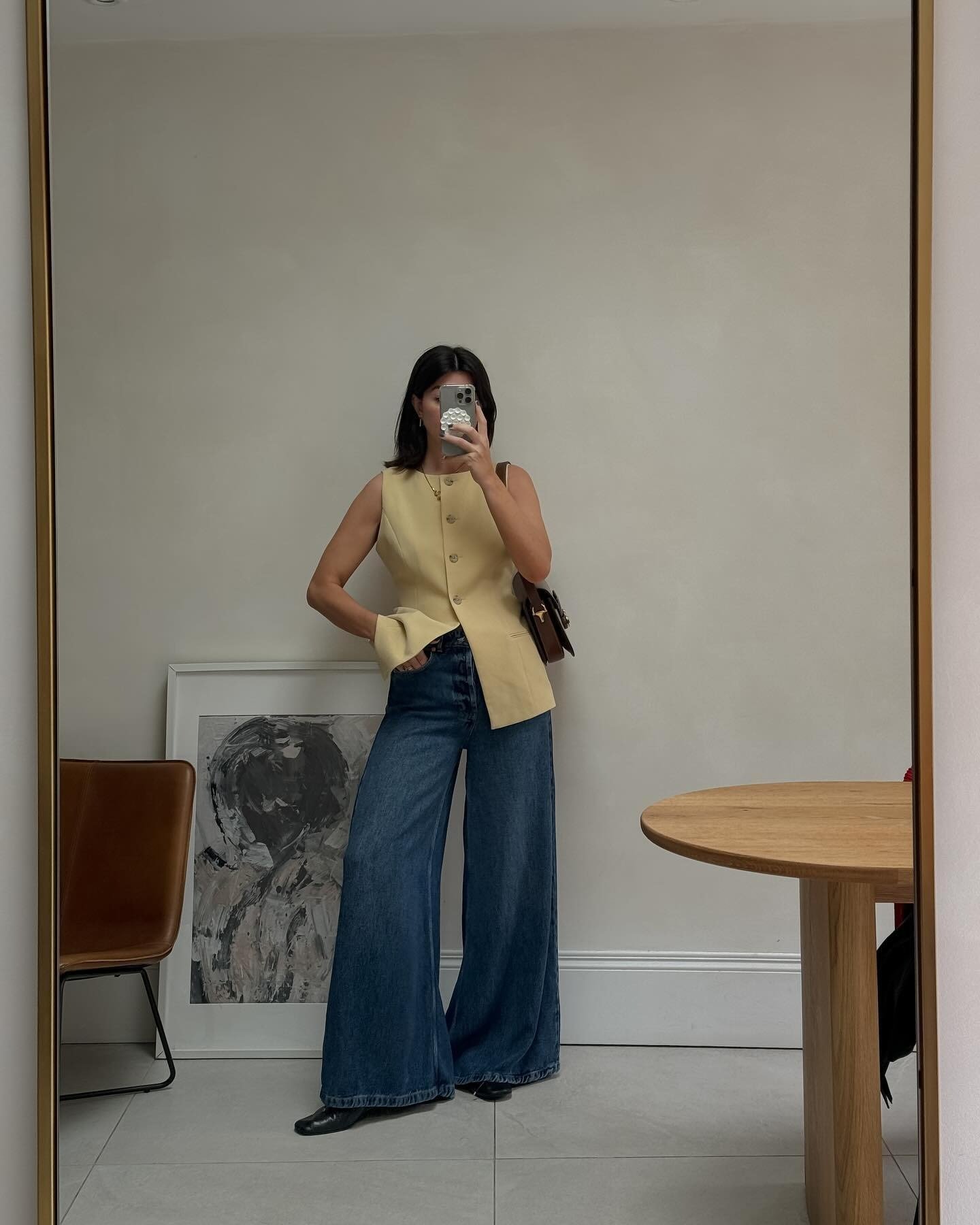 Modelo posa em frente ao espelho com look confortável e leve, usando colete bege estruturado e jeans azul escuro de