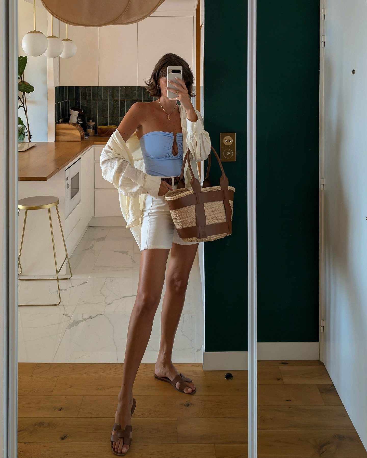 Modelo posa com looks elegantes para o verão usando top tomara que caia azul claro, saia branca, camisa leve e bolsa de