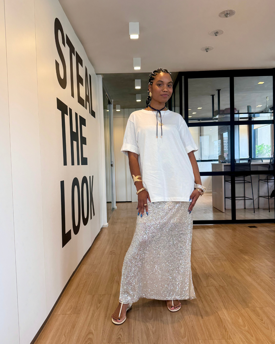 Modelo posa usando camiseta branca oversized e saia longa de paetês prateados, inspiração de looks estilosos para o fim de